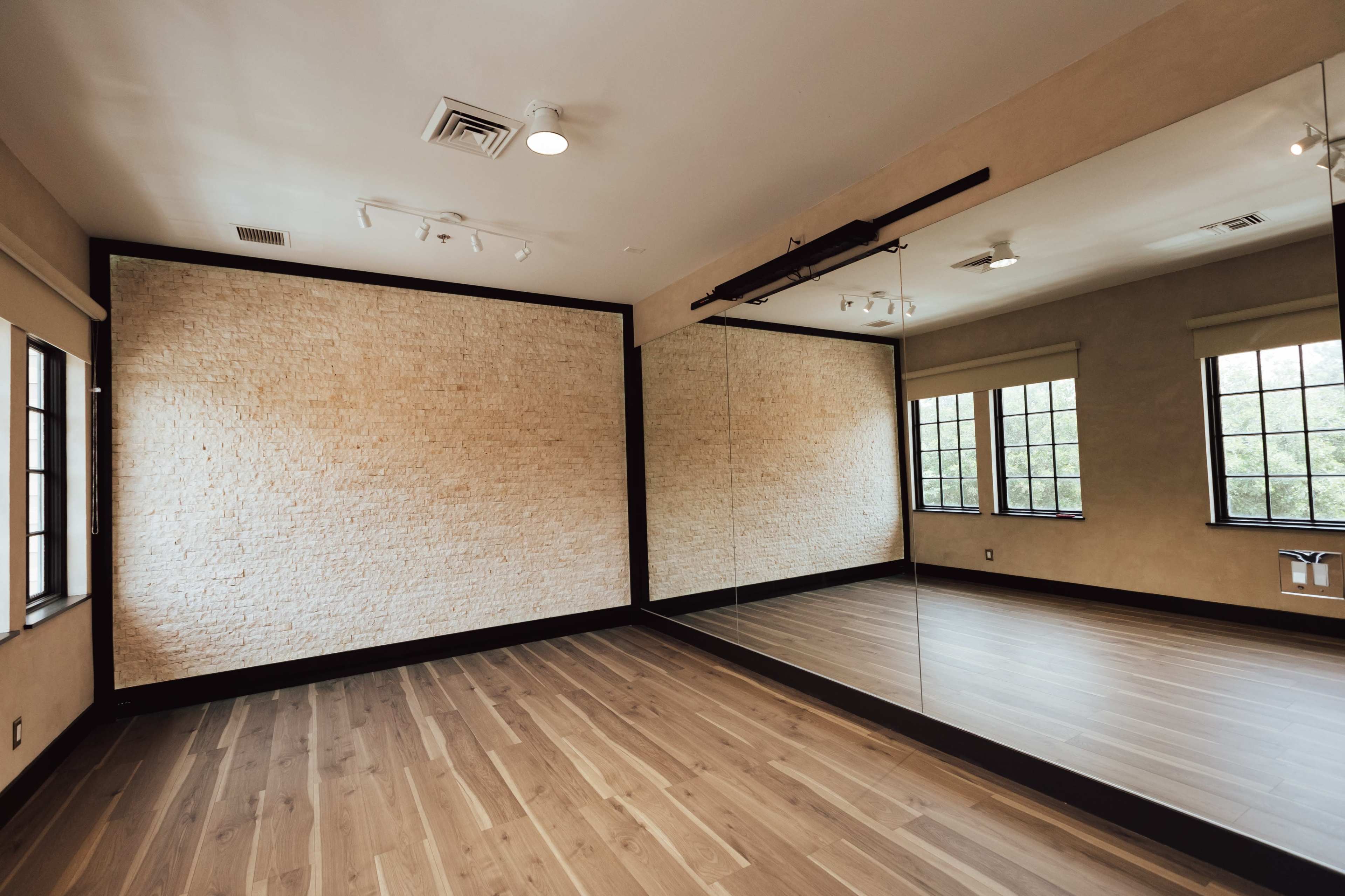 An interior room with a wooden floor, a stone wall on one side, and a large mirror on the opposite wall.