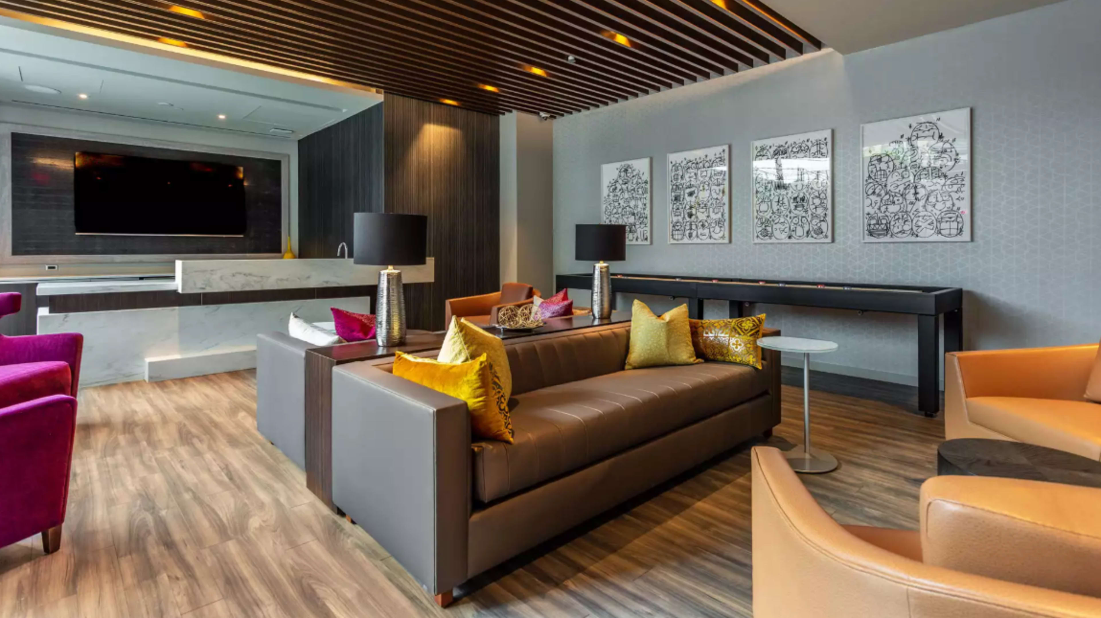 A modern lounge area with a gray sofa, colorful pillows, artwork on the walls, and a large television mounted above a marble surface.