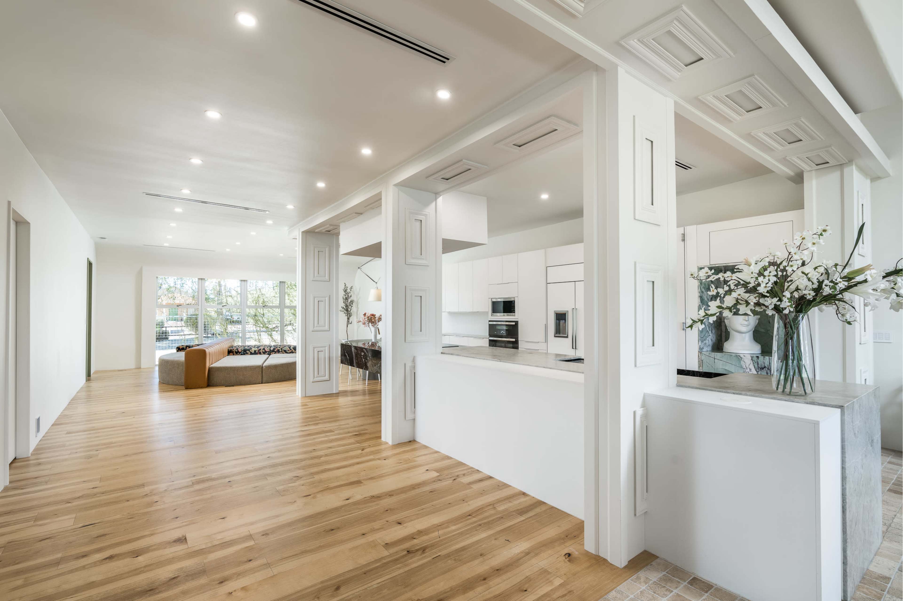 A modern, open-plan interior with a kitchen and living area, featuring hardwood floors and large windows.
