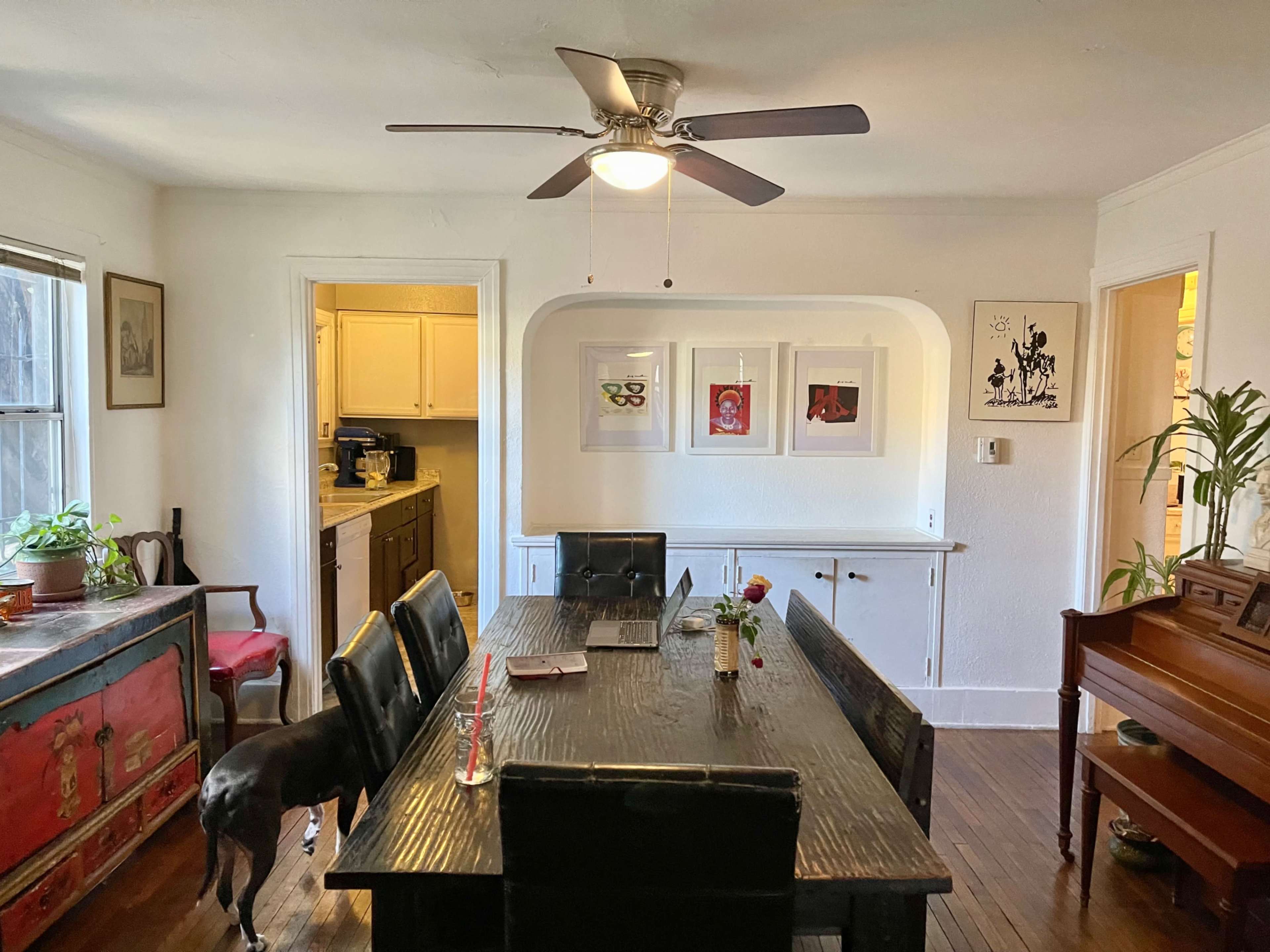 The room features a dining table surrounded by black chairs, with a ceiling fan above and framed artwork on the walls.