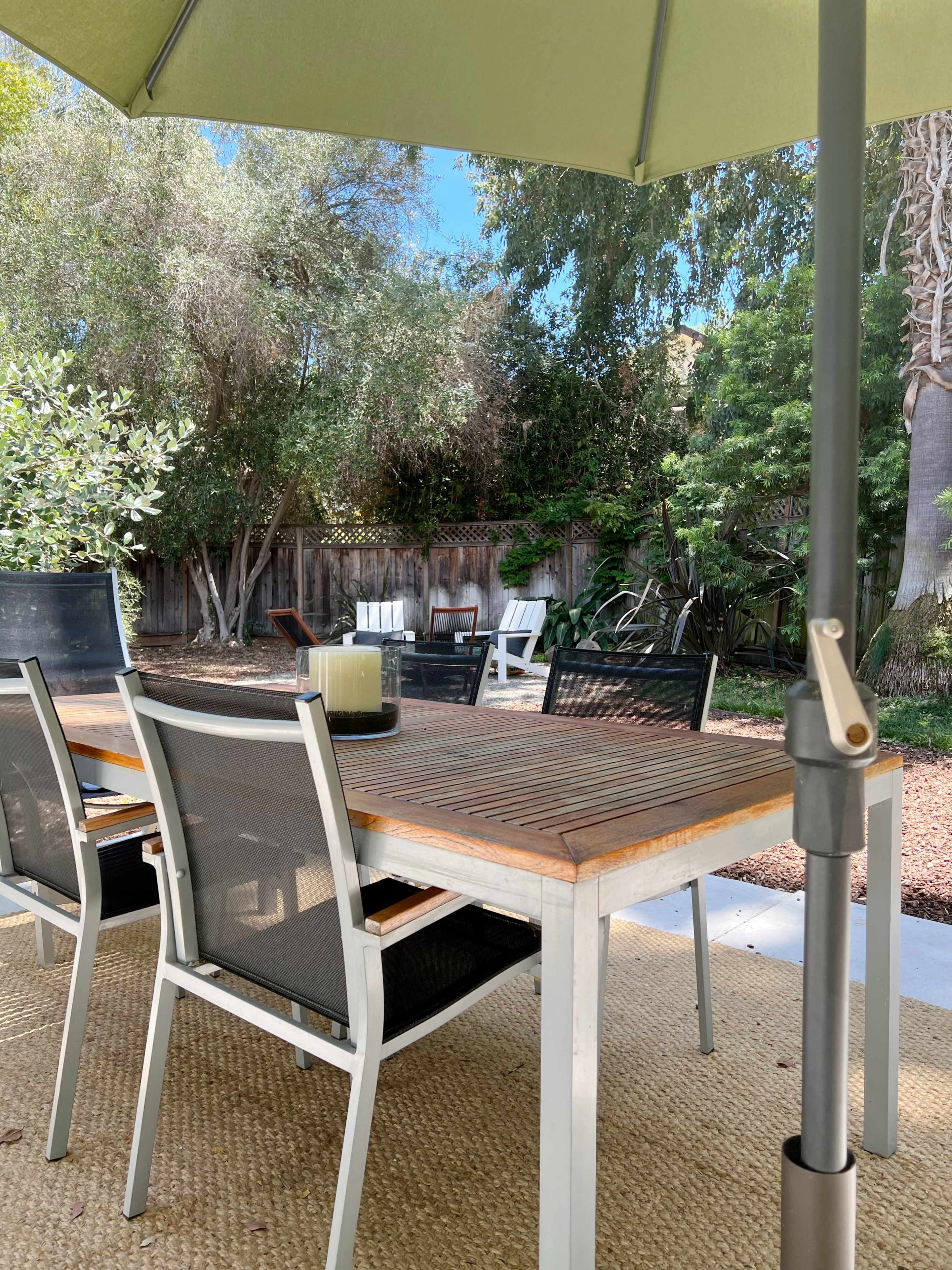 A patio table with chairs is set under an umbrella, overlooking a garden with seating areas and lush greenery.