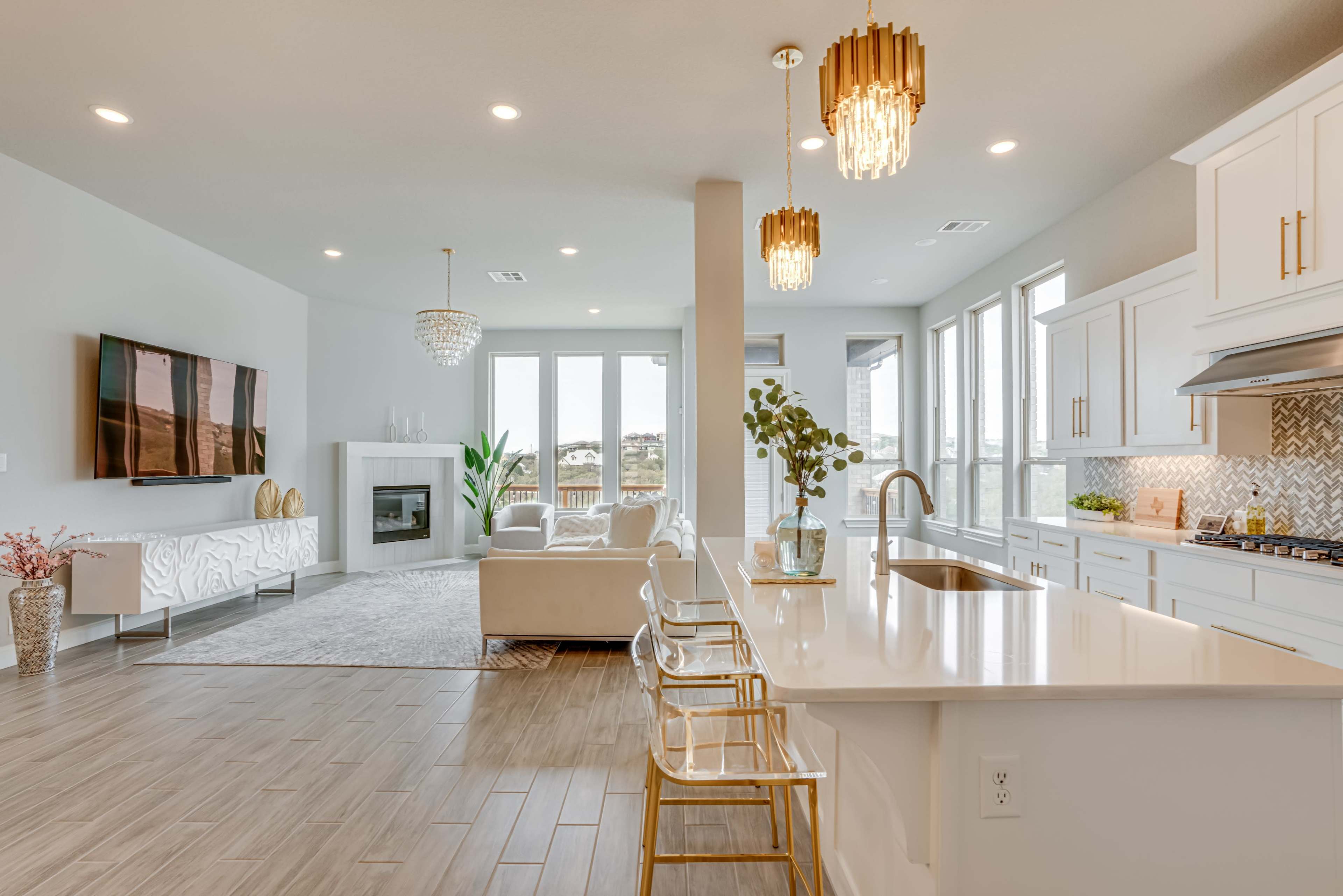 A modern open-concept living space featuring a kitchen with white cabinetry, a dining area with clear chairs, and a comfortable sitting area with large windows.