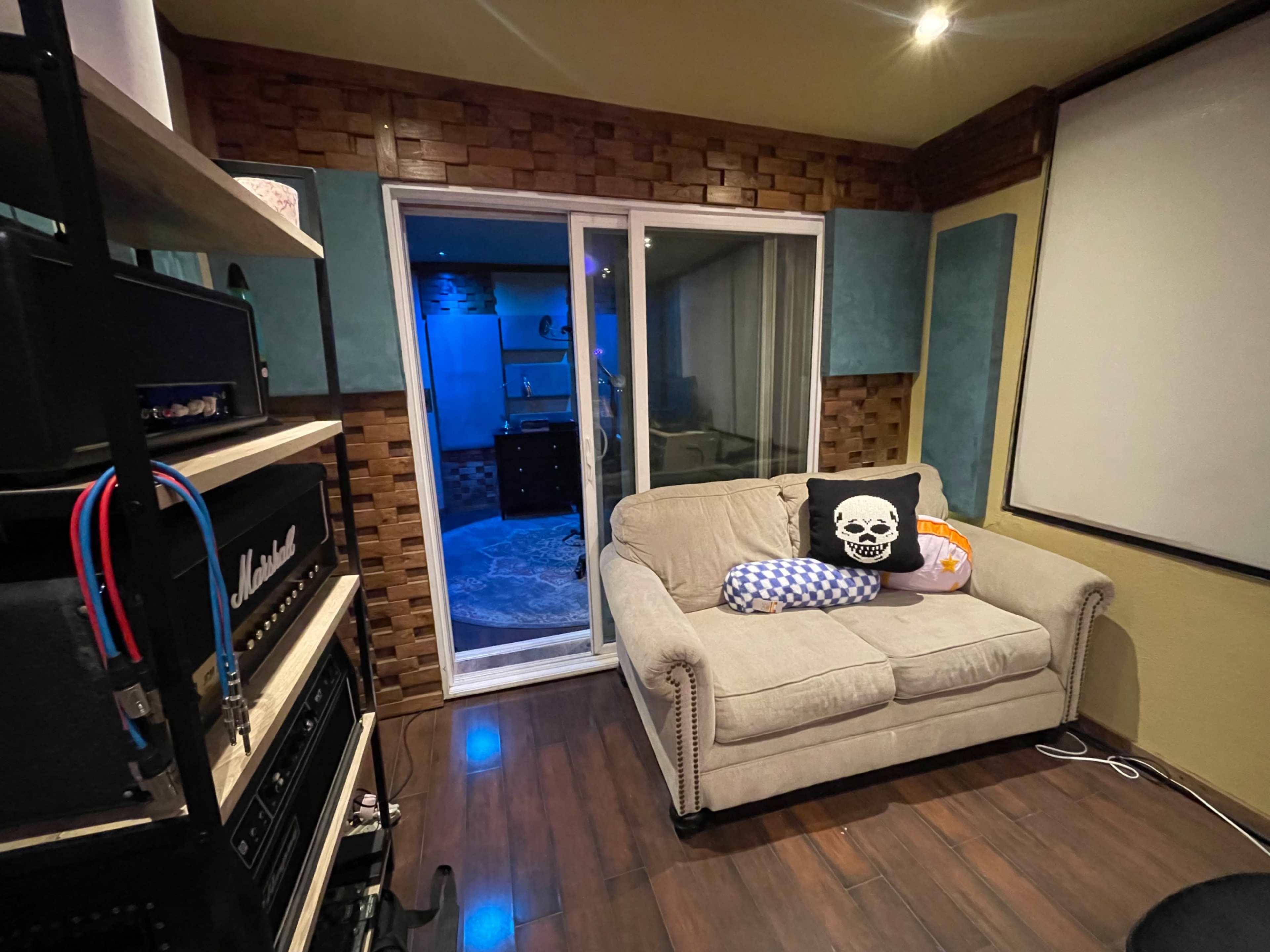 The image shows a cozy room with a sofa, an open glass door leading to another area, and audio equipment on shelves.