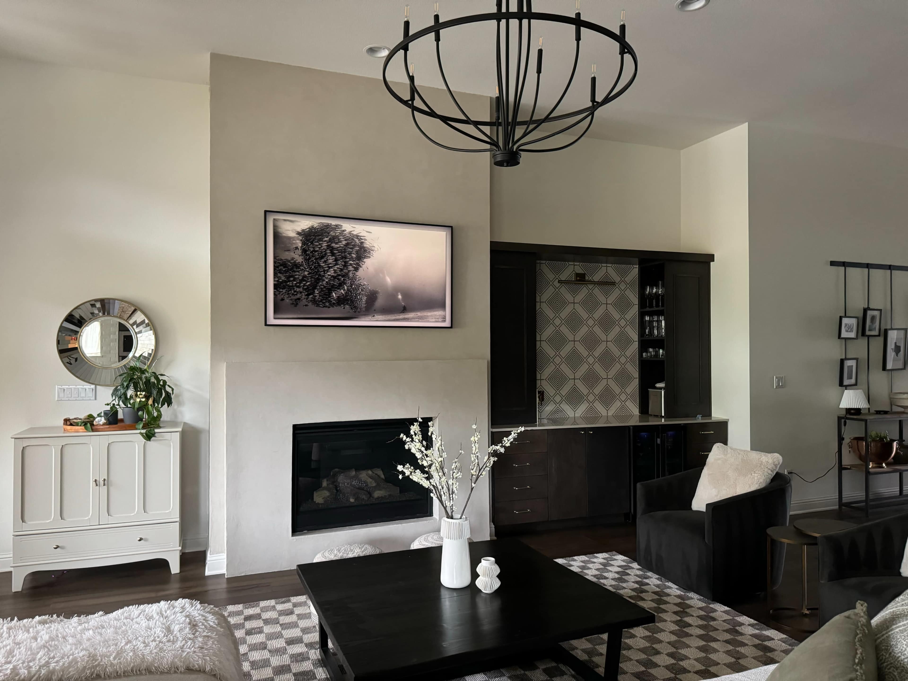 The image shows a modern living room with a wall-mounted television above a fireplace, a dark wood coffee table, and a light-colored couch set against neutral walls.