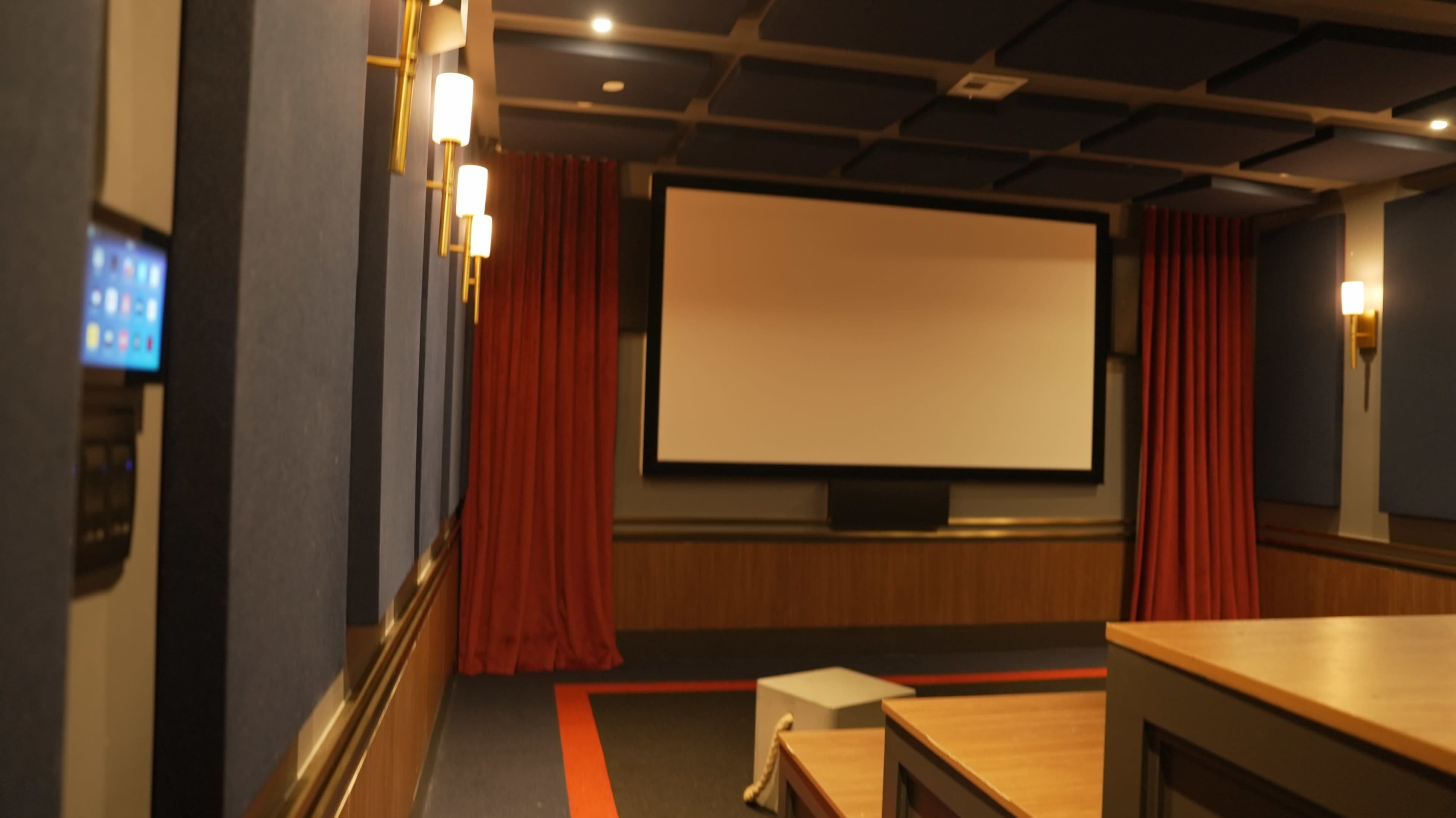 The image shows a home theater room featuring a large projection screen, red curtains, and wood-paneled walls with modern lighting.