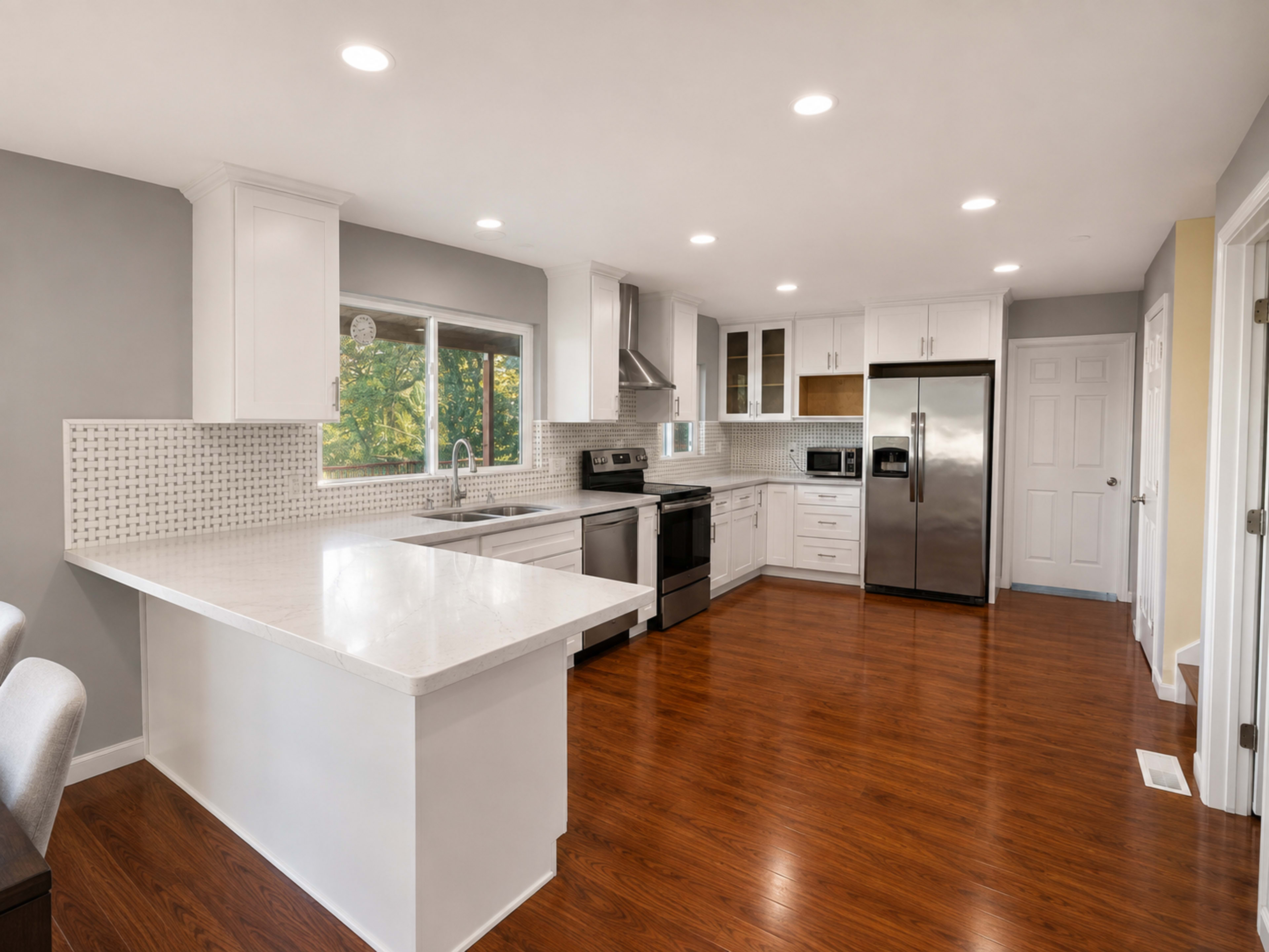 The image shows a modern kitchen with white cabinetry, stainless steel appliances, and dark wooden flooring.