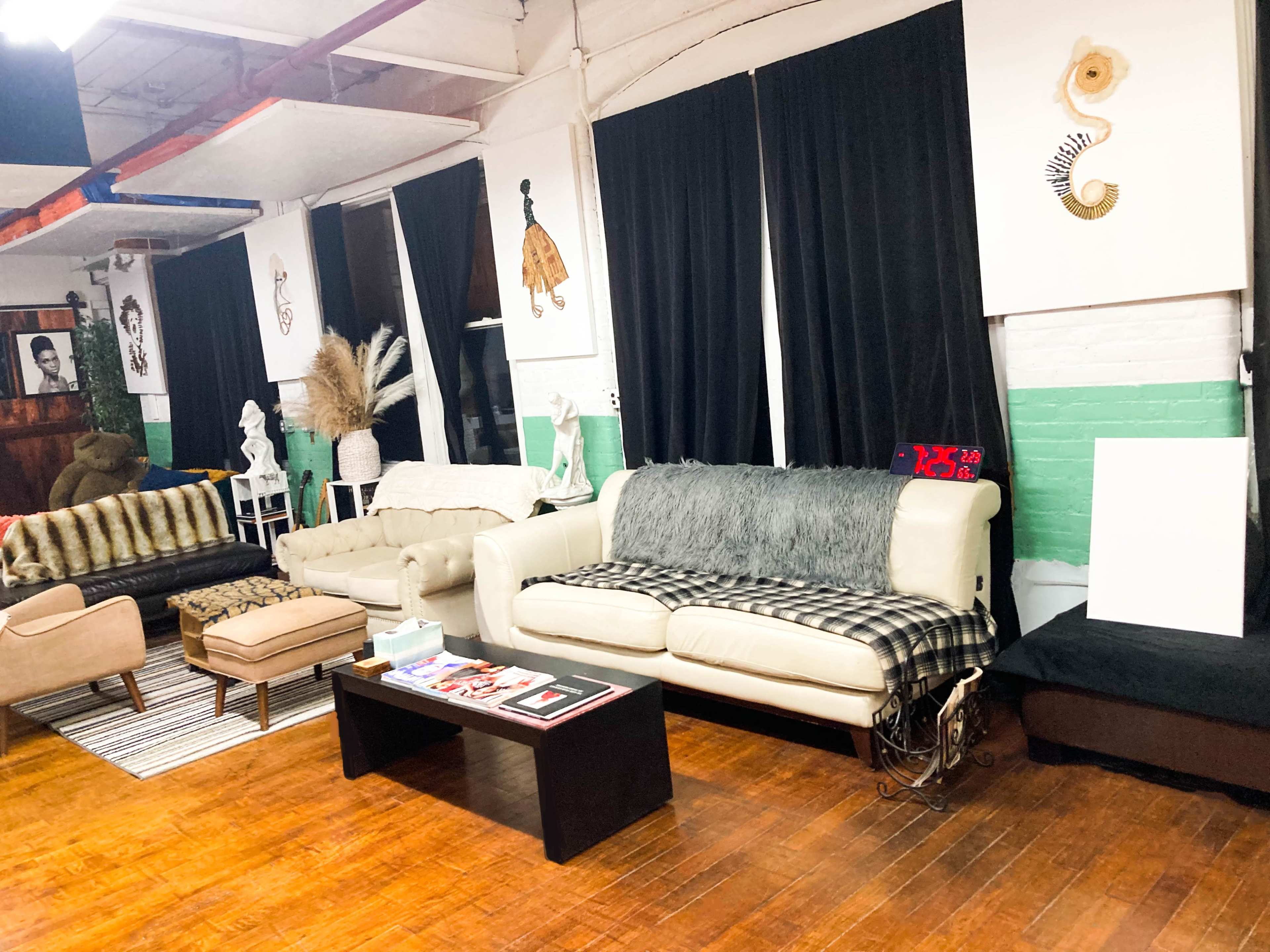 A spacious lounge area with several sofas arranged around a coffee table, surrounded by artworks on the walls and large curtains.