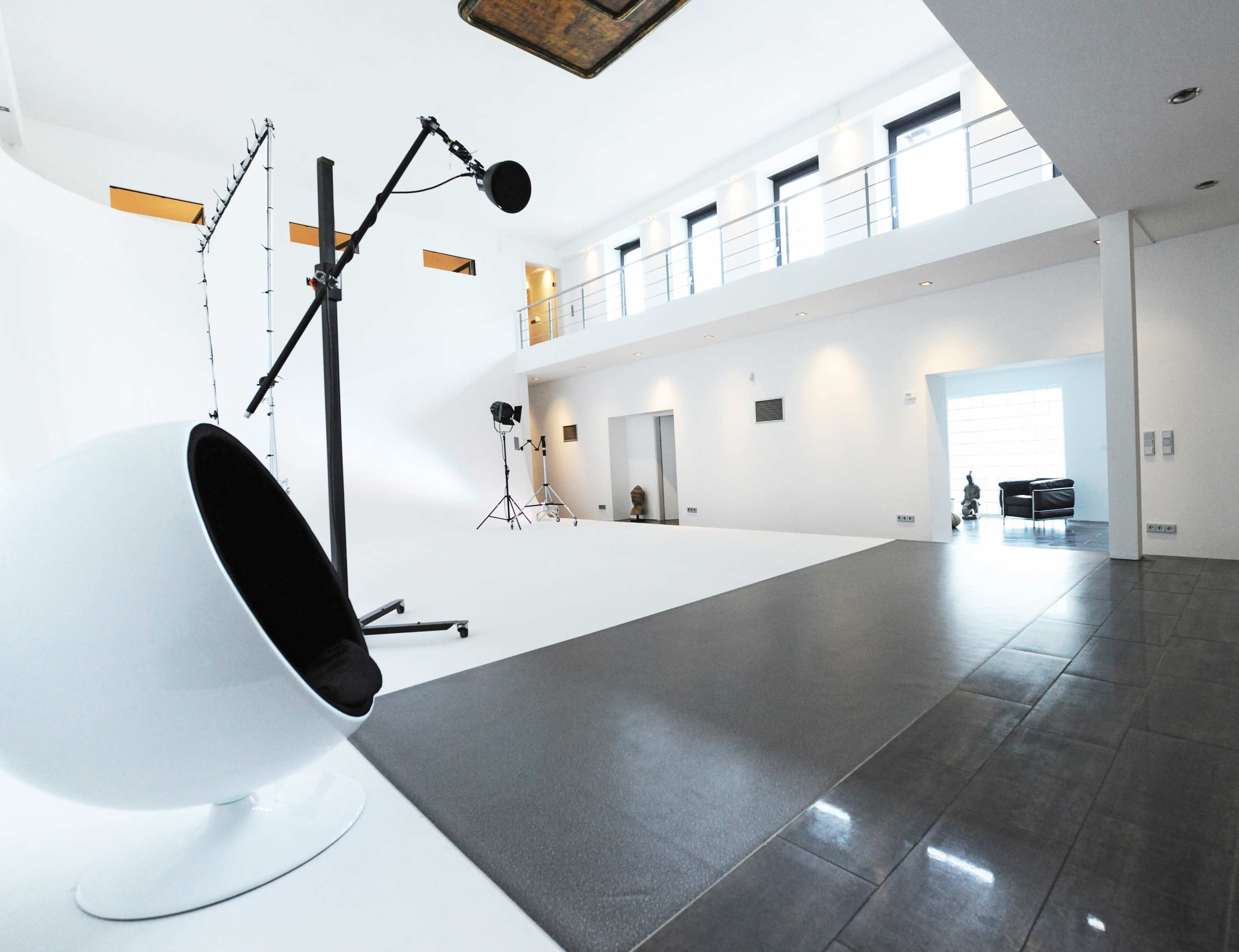 The image shows a spacious, modern photography studio with a large white backdrop, a microphone on a stand, and various lighting equipment.