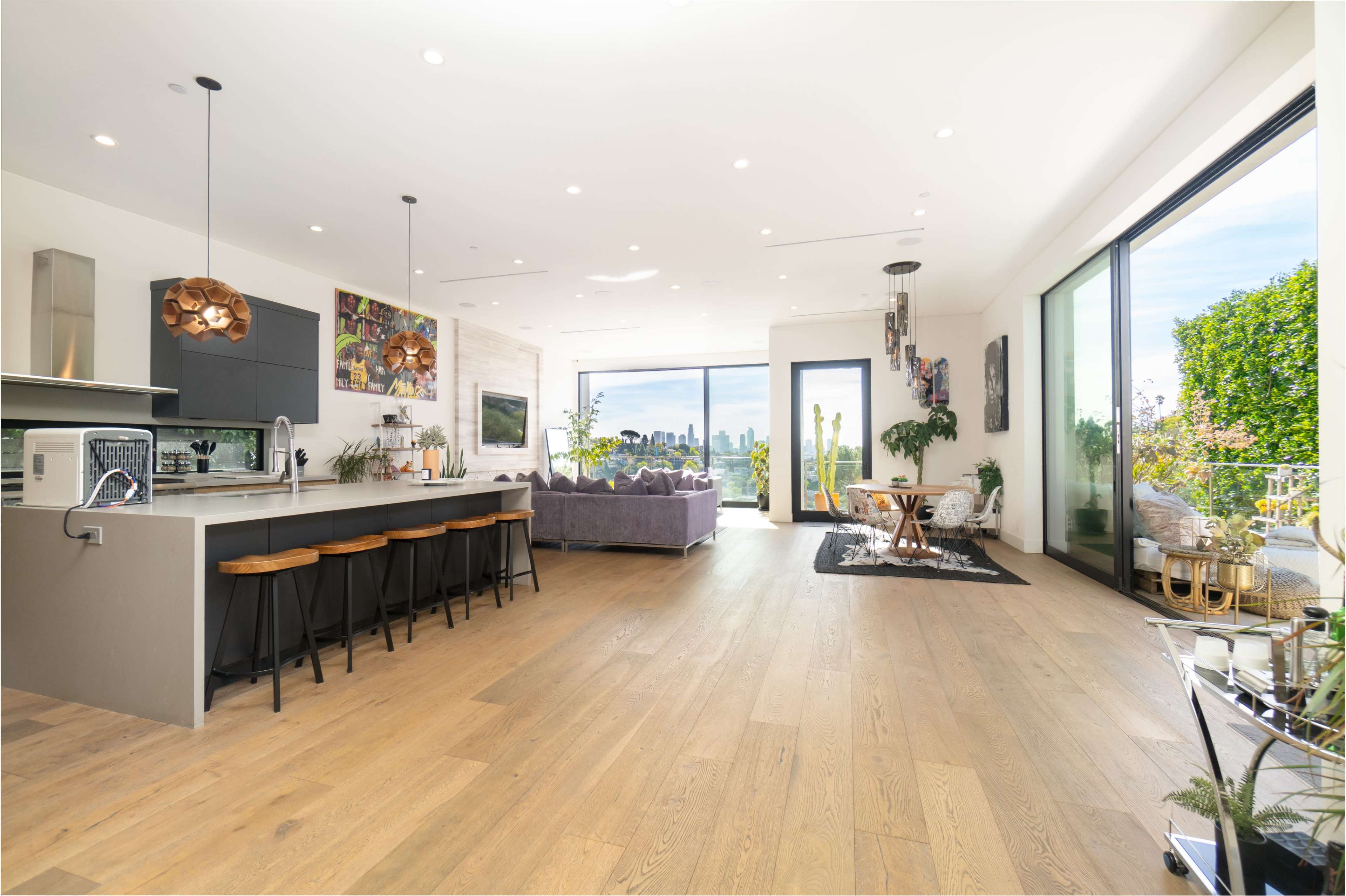 A modern open-concept living space featuring a kitchen island, dining area, and lounge with large windows overlooking a city skyline.
