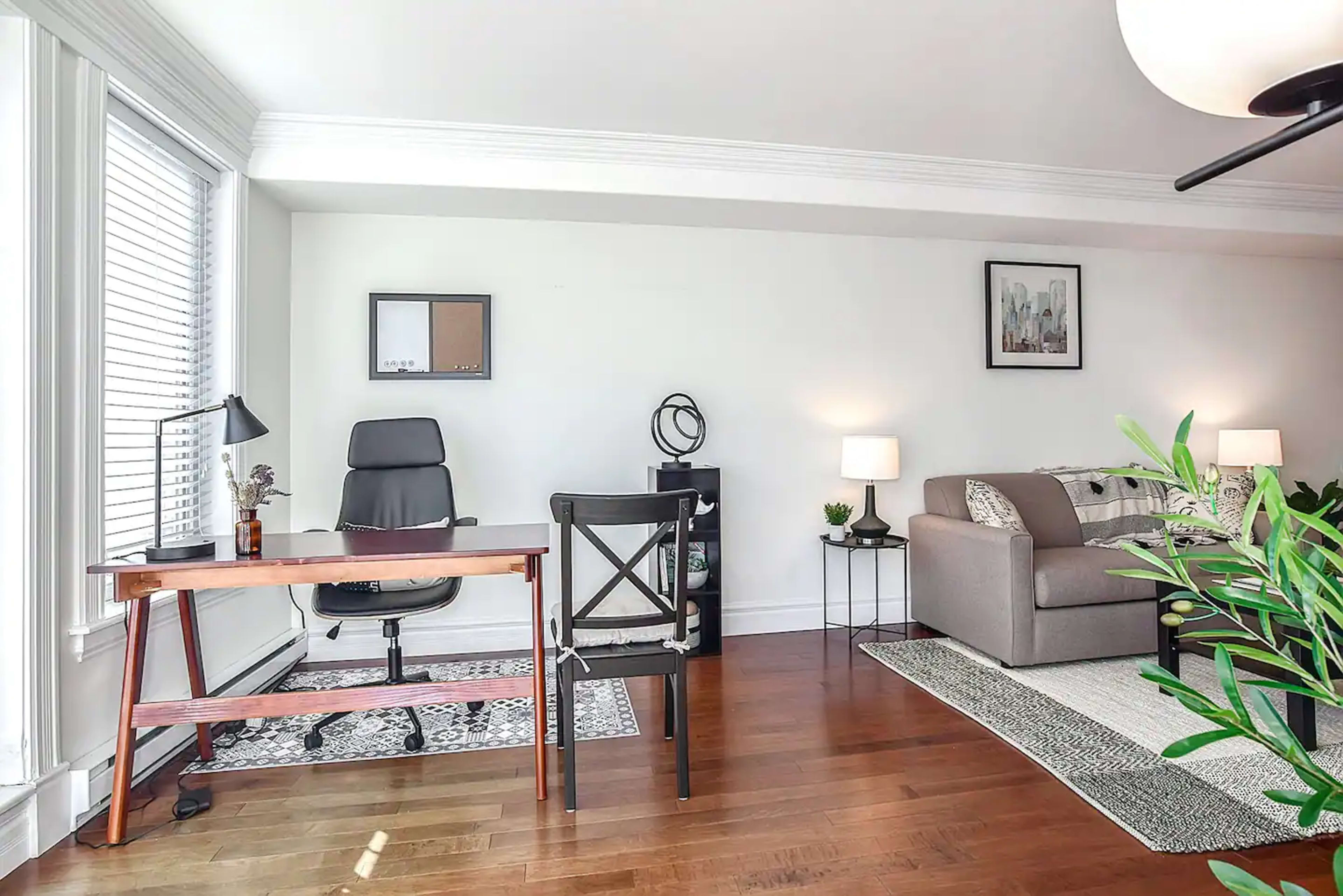 A well-lit living space featuring a desk and chair setup, a sofa, and decorative elements such as plants and lamps.