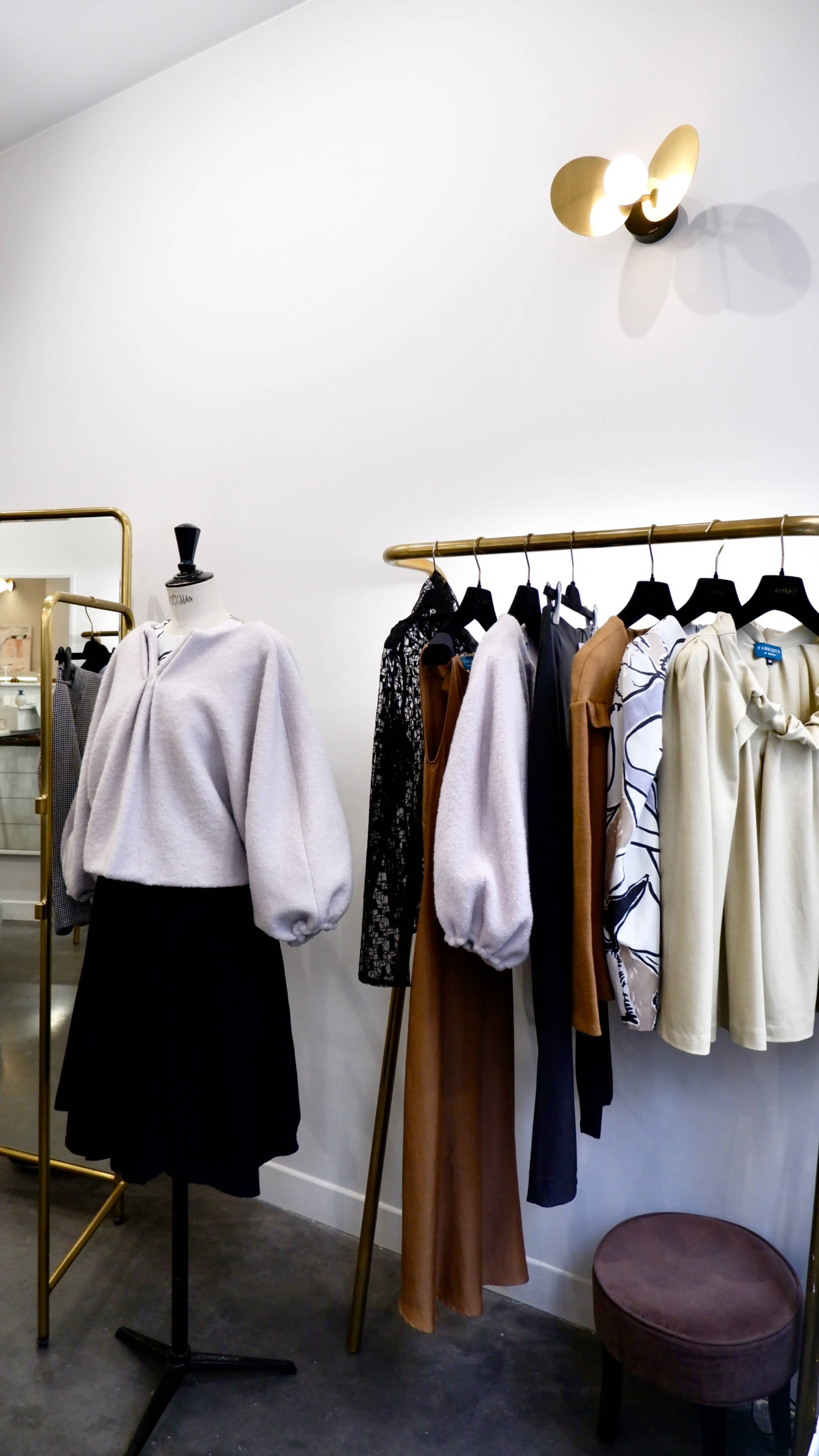 A clothing display in a boutique featuring various garments hanging on racks, alongside a mannequin dressed in a sweater and skirt.