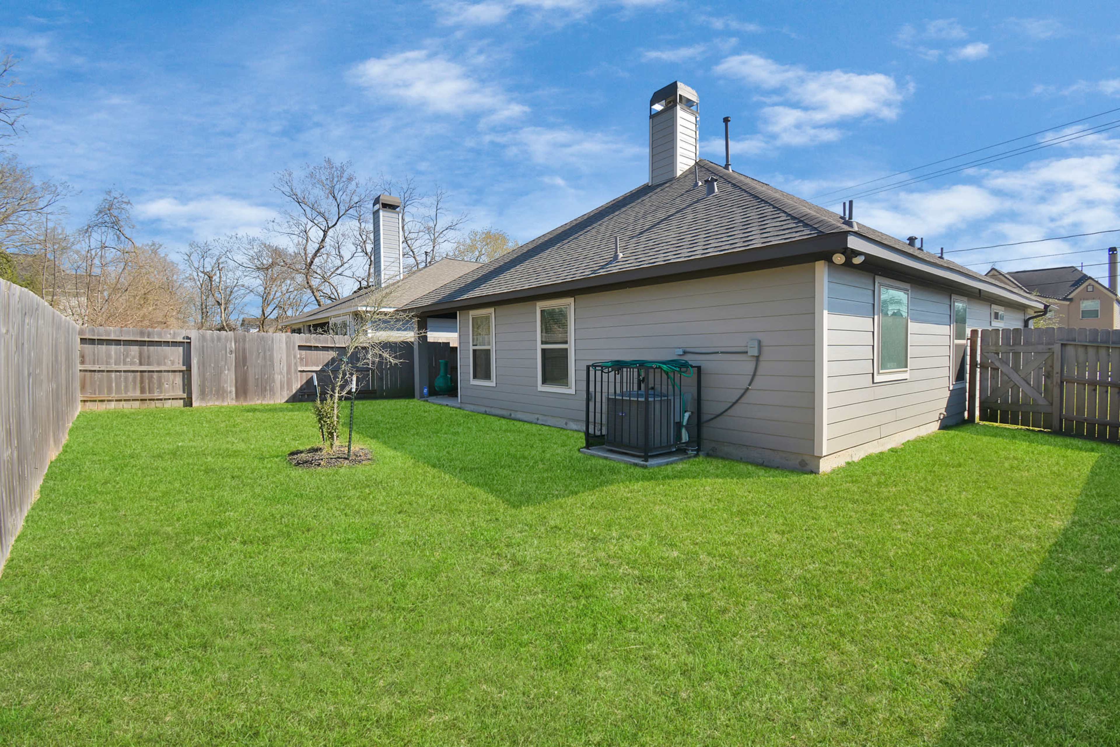 A backyard featuring a well-maintained lawn, a single small tree, and a house with two chimneys and a water connection on one side.