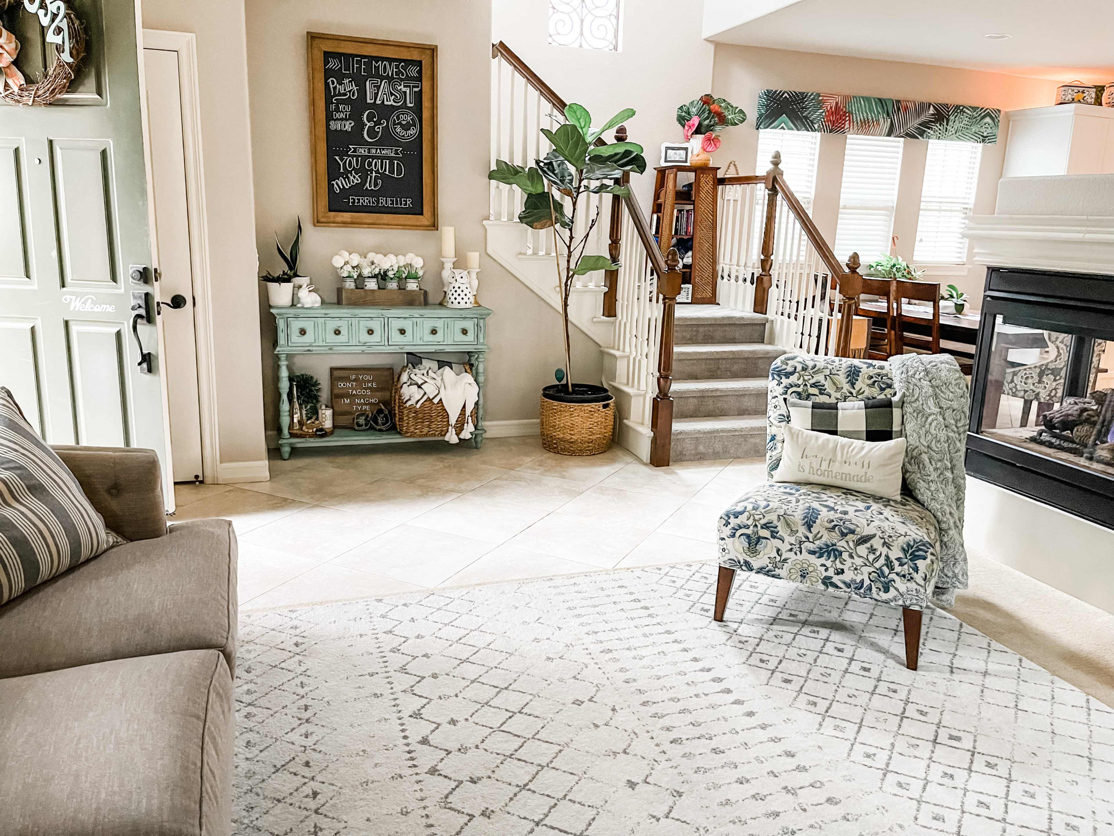 The living room features a light-colored sofa, a patterned armchair, a decorative console table, and a staircase leading to an upper level.