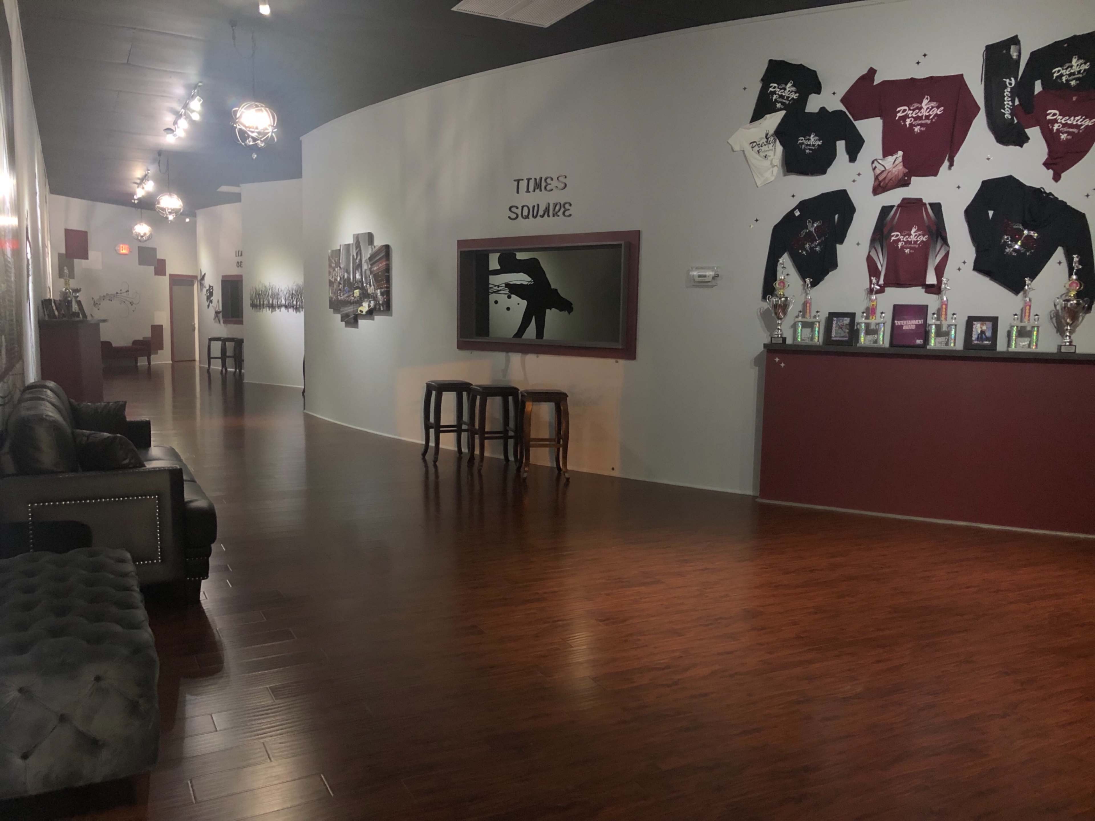 The interior of a dance studio features a curved wall displaying shirts, a TV screen, and a row of trophies along with a seating area.