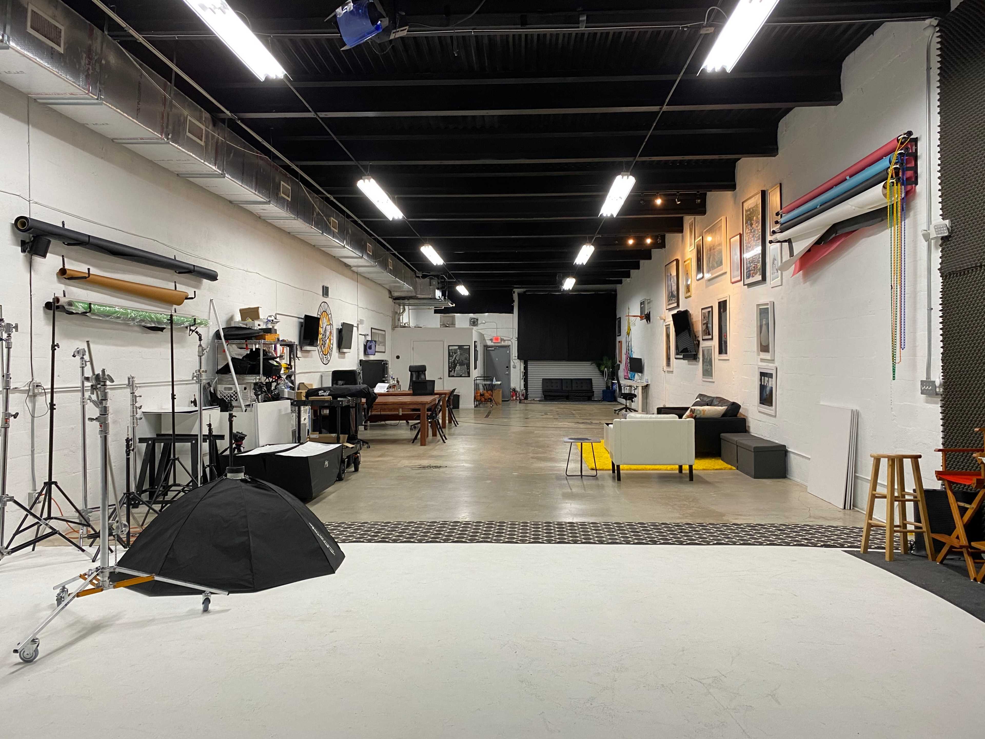 A spacious photography studio with various equipment, furniture, and a backdrop area along the walls.
