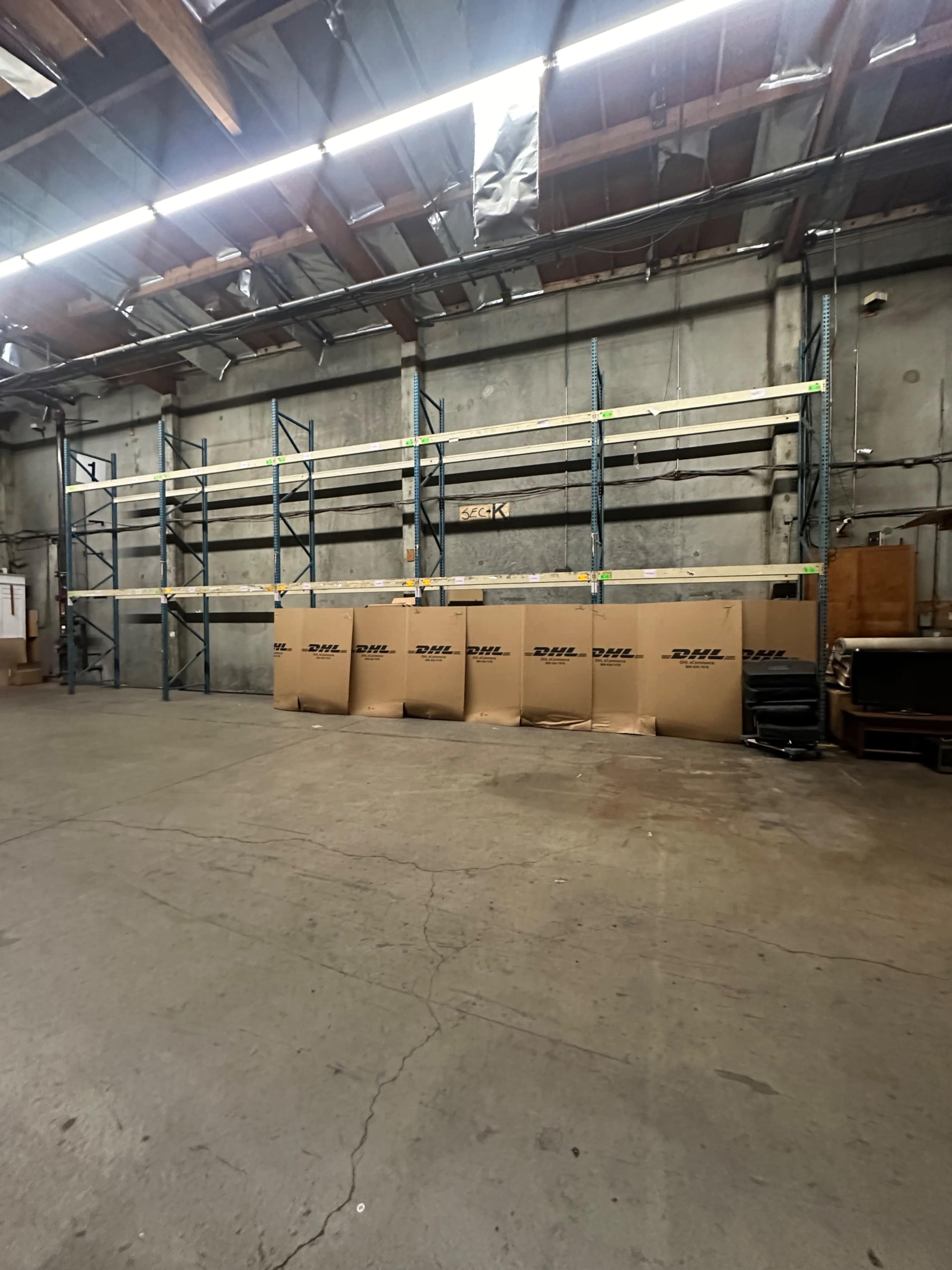 The image shows a warehouse interior with metal shelving on one wall and several large boxes arranged in front of it.