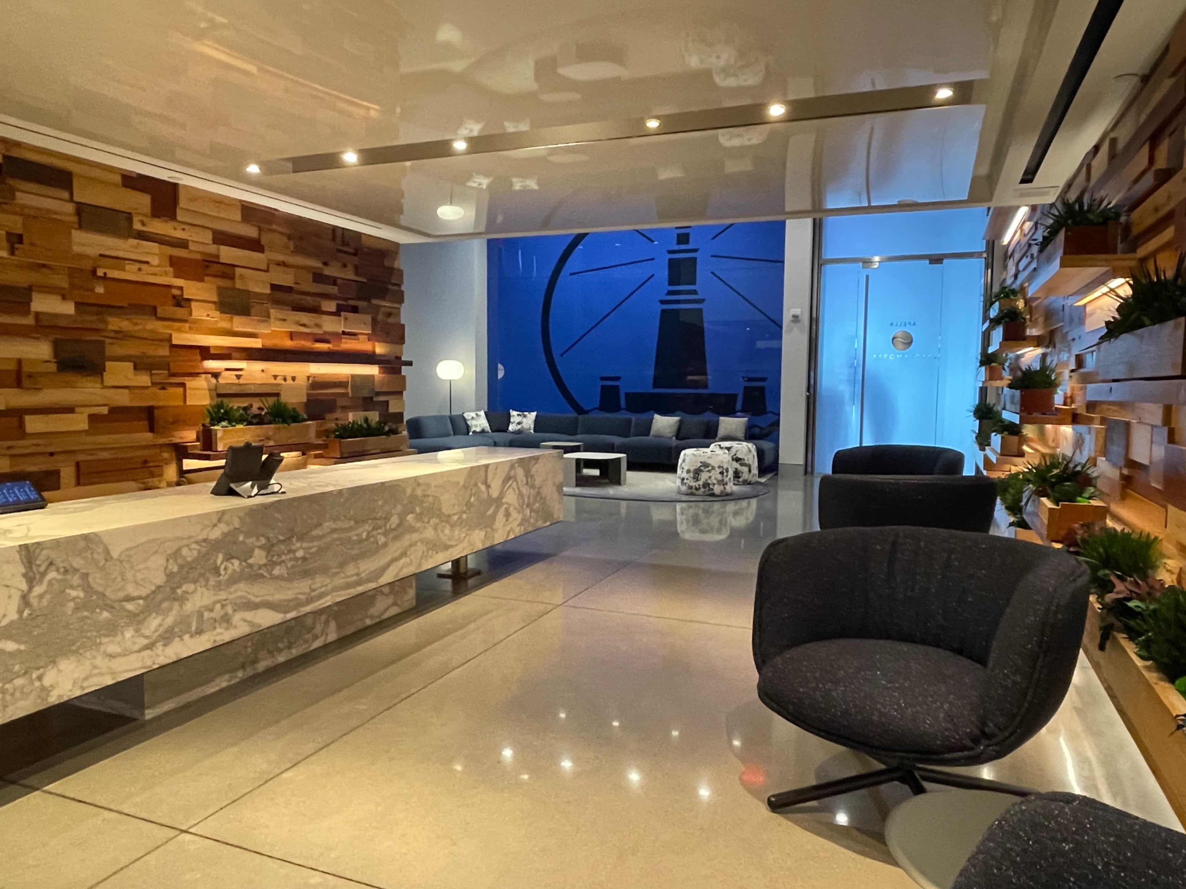 The image shows a modern reception area with a marble front desk, wooden accent walls, a blue mural, and contemporary seating arrangements.