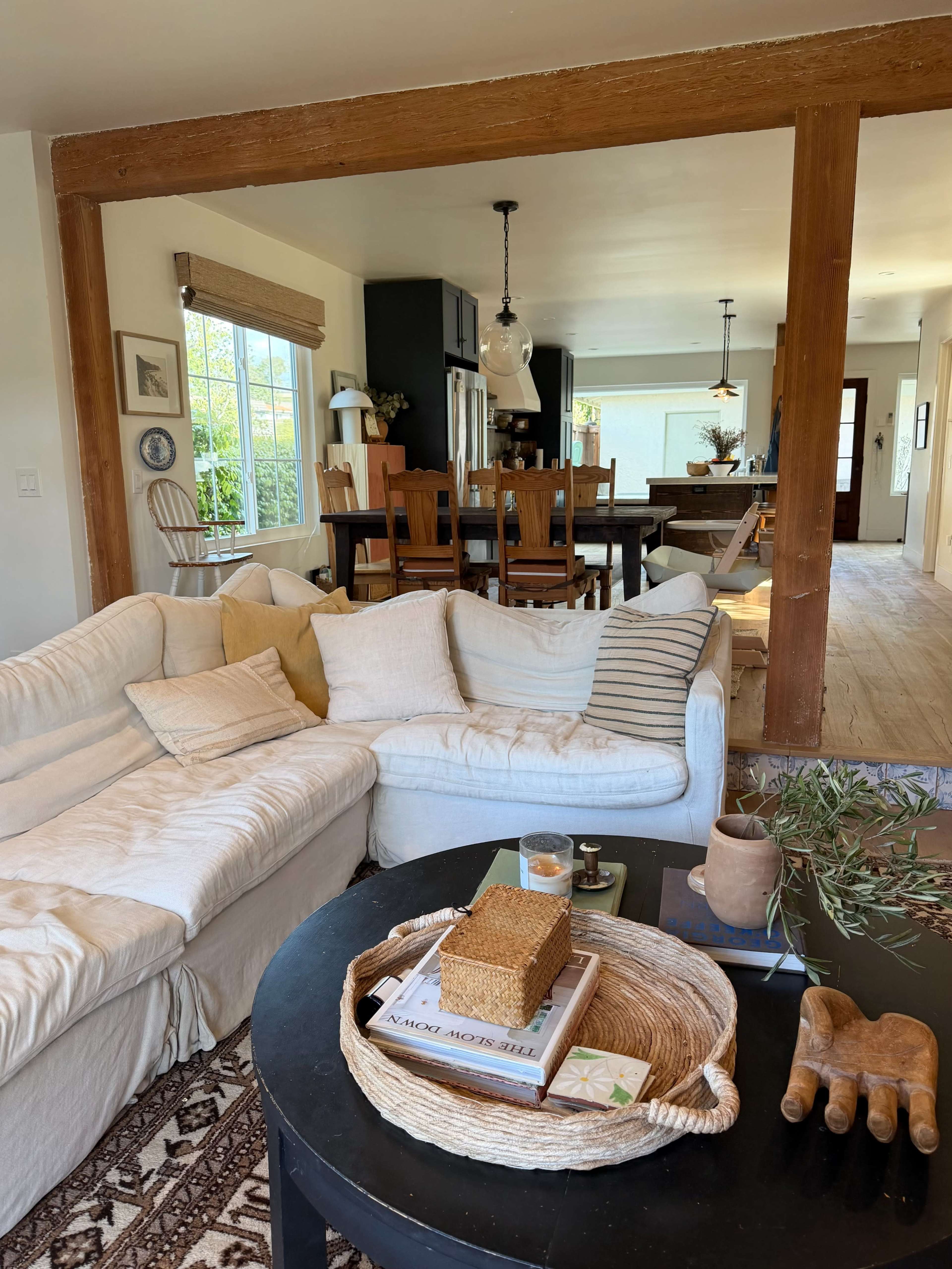 The image shows a cozy living room with a white sectional sofa, a black coffee table adorned with books and decorative items, and a view into a connected dining area with wooden furniture.