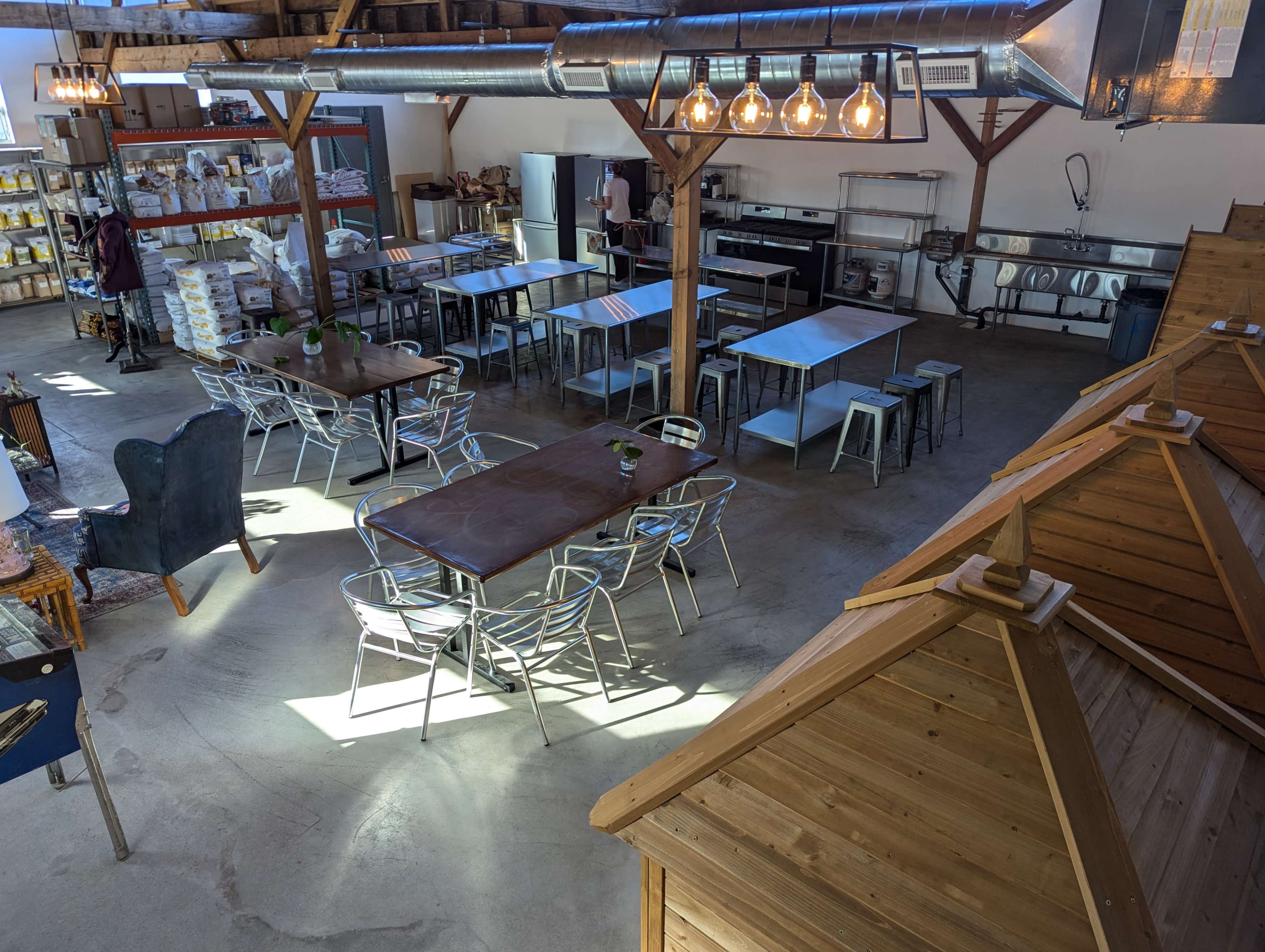 A spacious interior with several tables, wooden structures resembling small houses, and a kitchen area in a commercial setting.