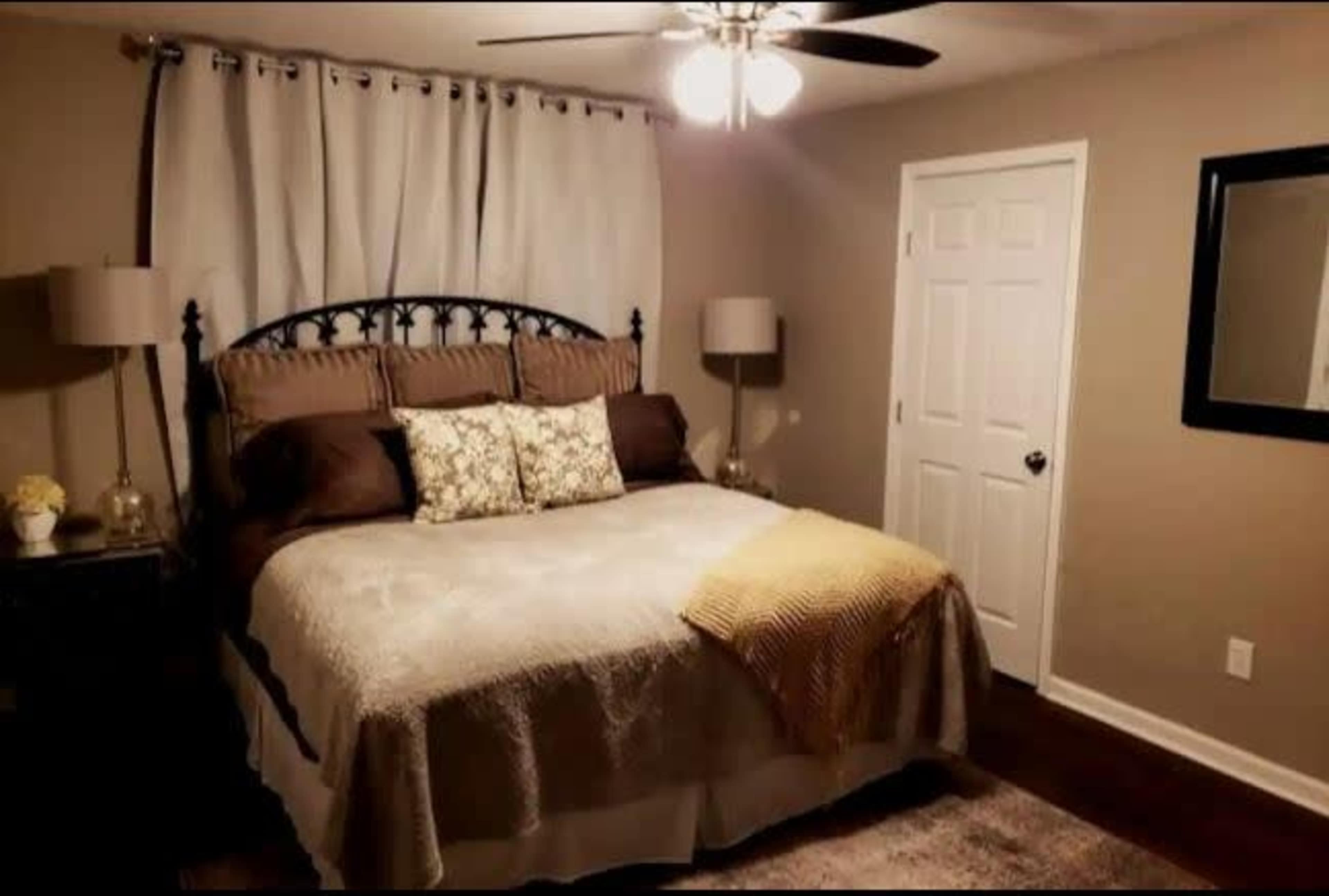 A neatly arranged bedroom featuring a large bed with decorative pillows, two bedside lamps, and a dresser with a mirror, all set against a neutral wall color.