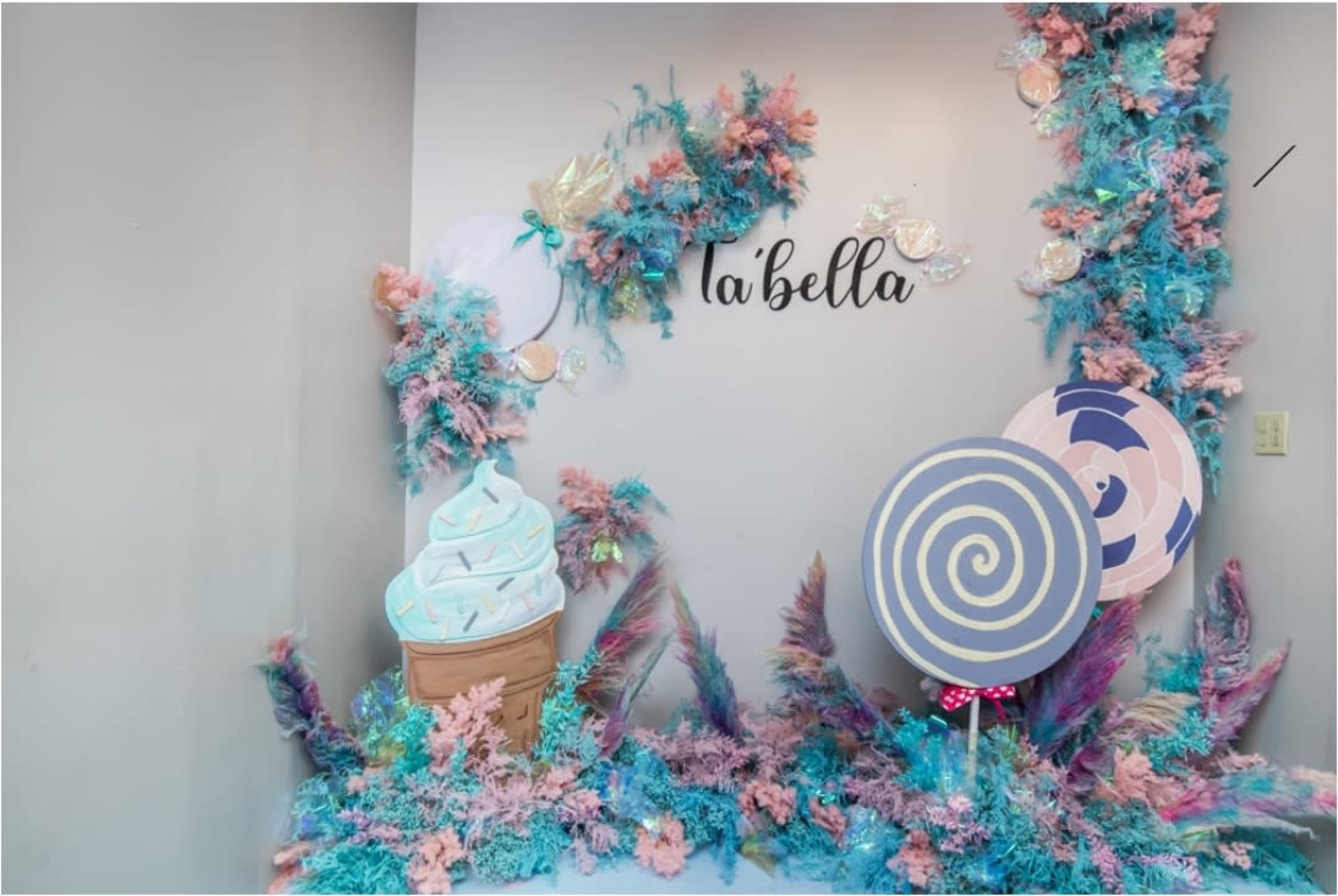A decorative backdrop featuring pastel-colored ice cream cones, large lollipops, and colorful foliage for a themed event.