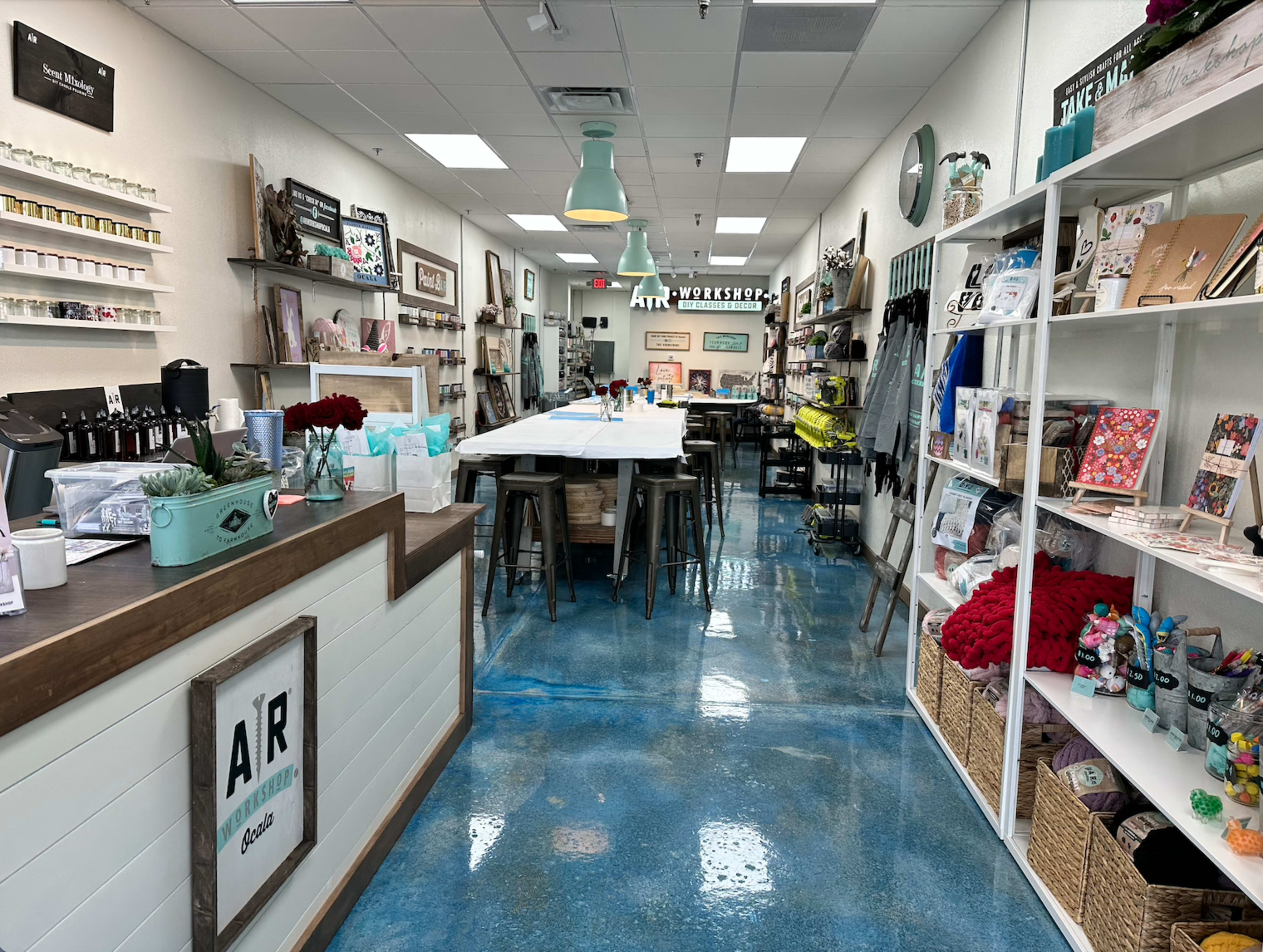 The interior of a crafting store with a long table in the center, surrounded by shelves displaying various art supplies and finished projects.