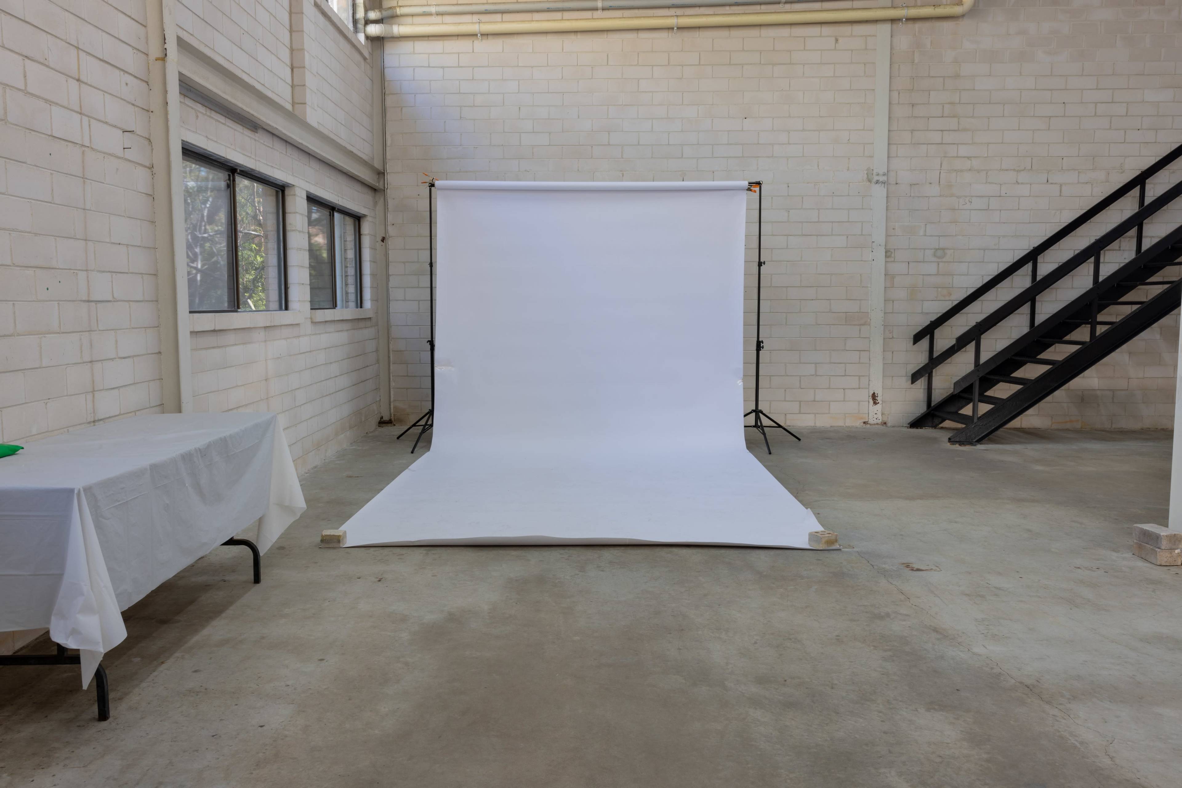 An empty studio space features a white backdrop on the floor, illuminated by natural light from large windows.
