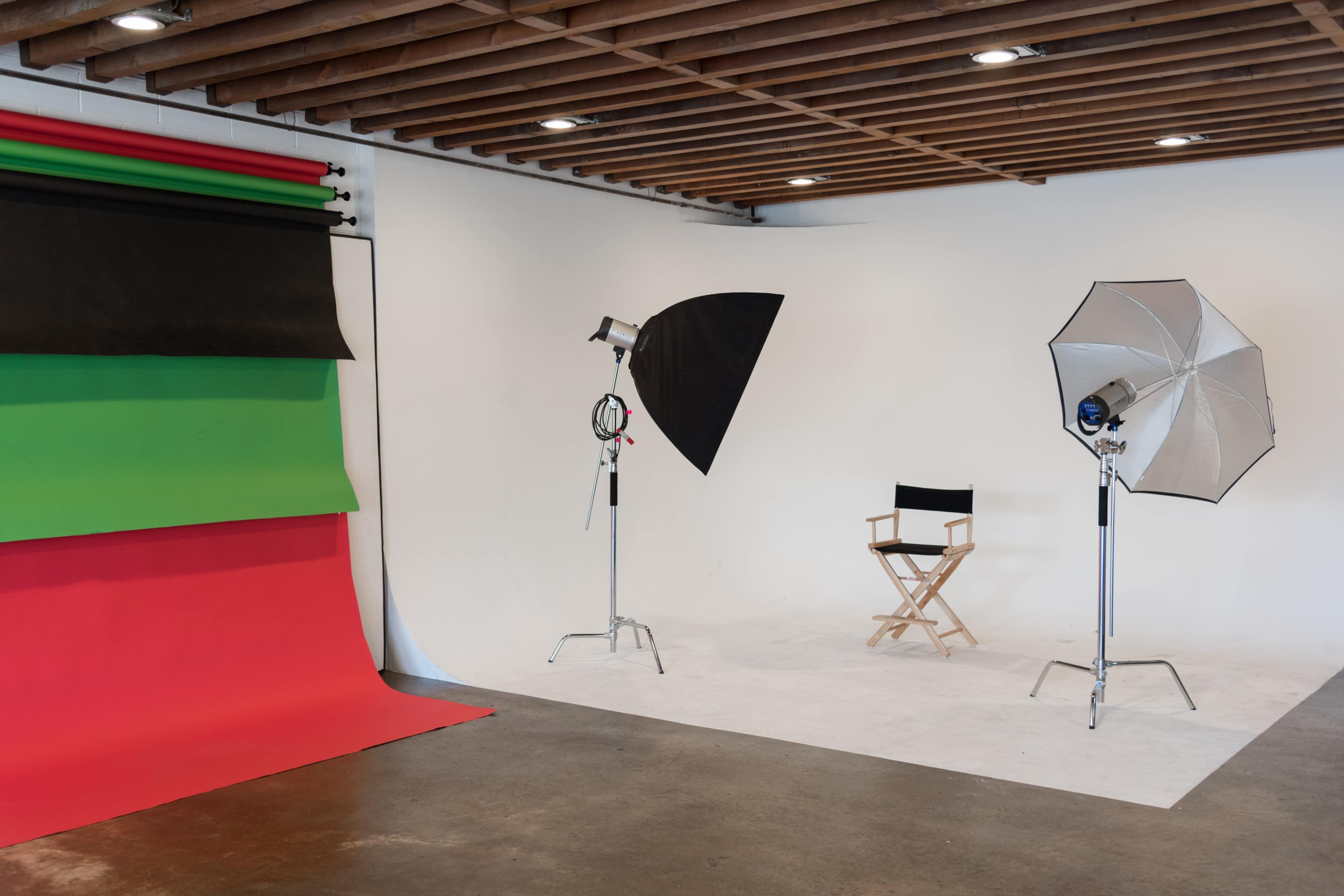 The image shows a photography studio with a green and red backdrop, two lighting setups, and a director's chair against a white wall.
