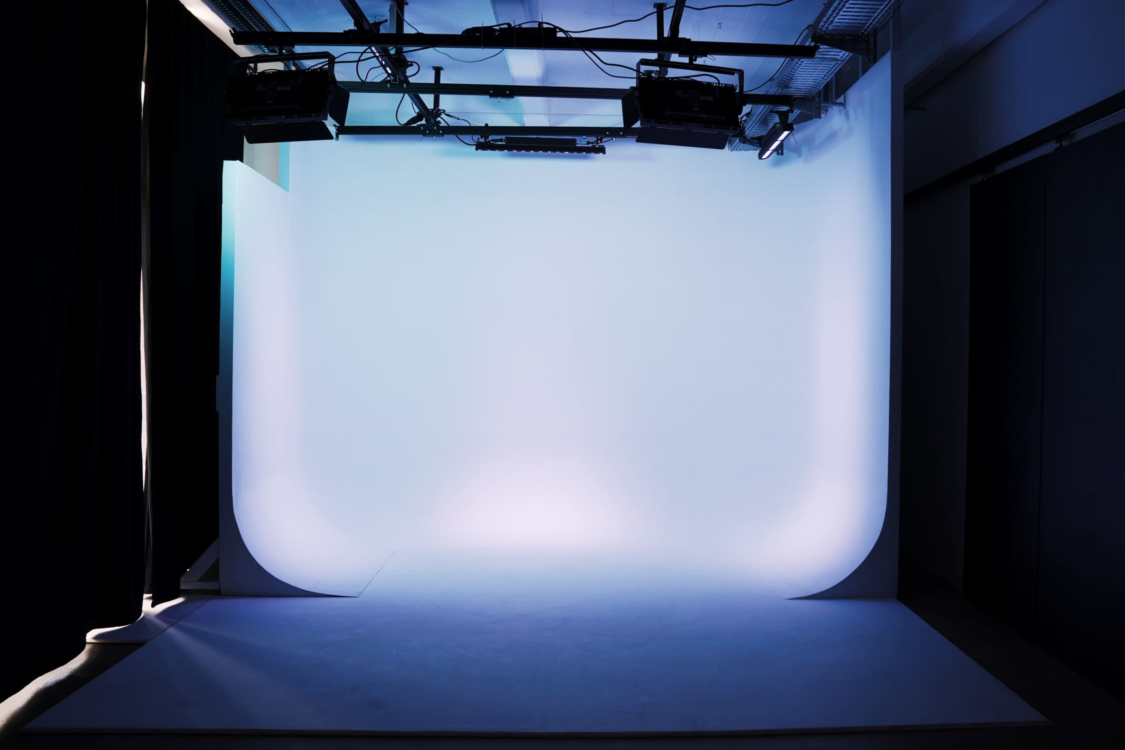 The image shows an empty photography studio with a curved white backdrop and soft lighting.