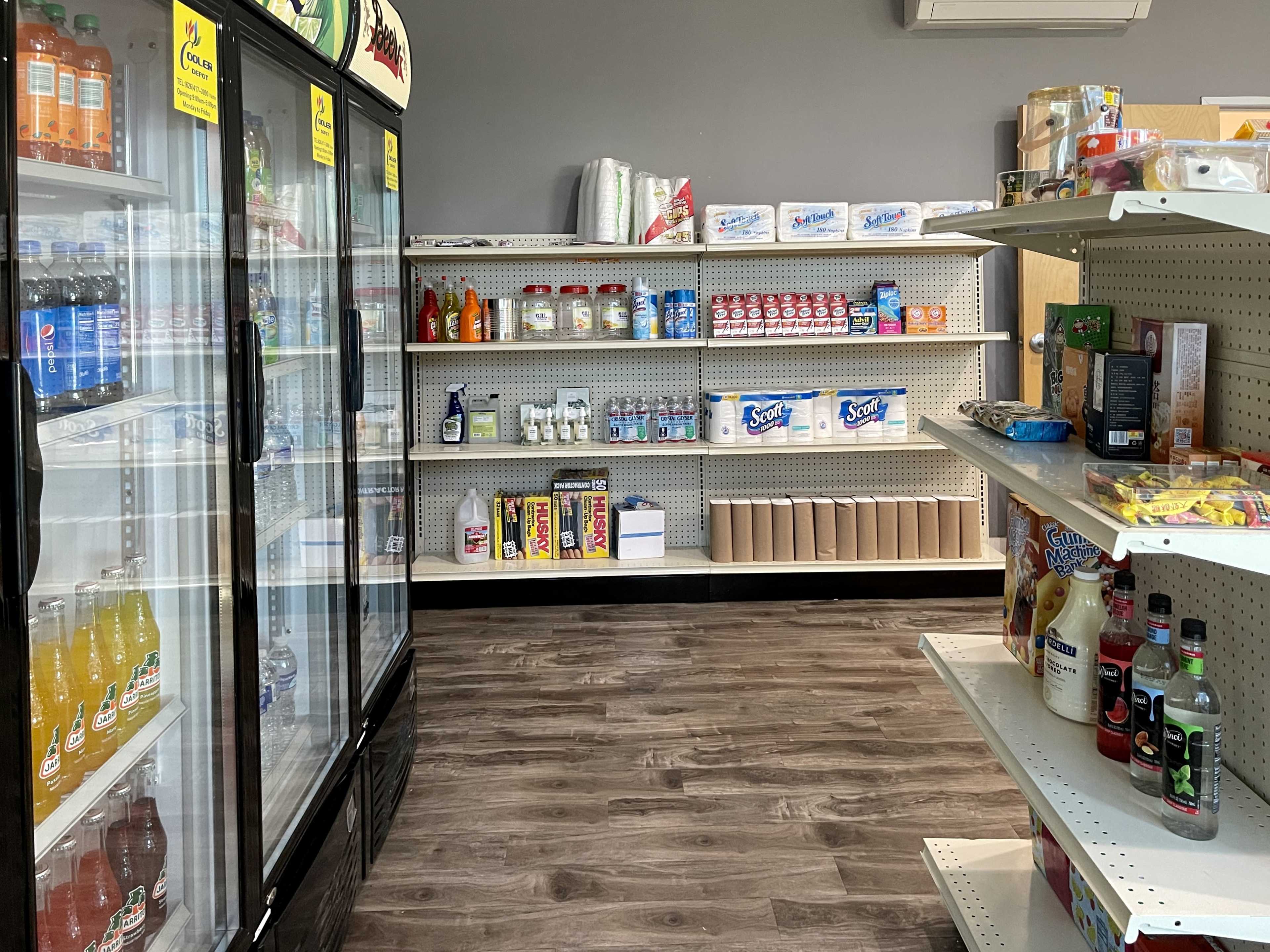 The interior of a convenience store with coolers on the left, shelves stocked with beverages and snacks, and a clear aisle in the center.