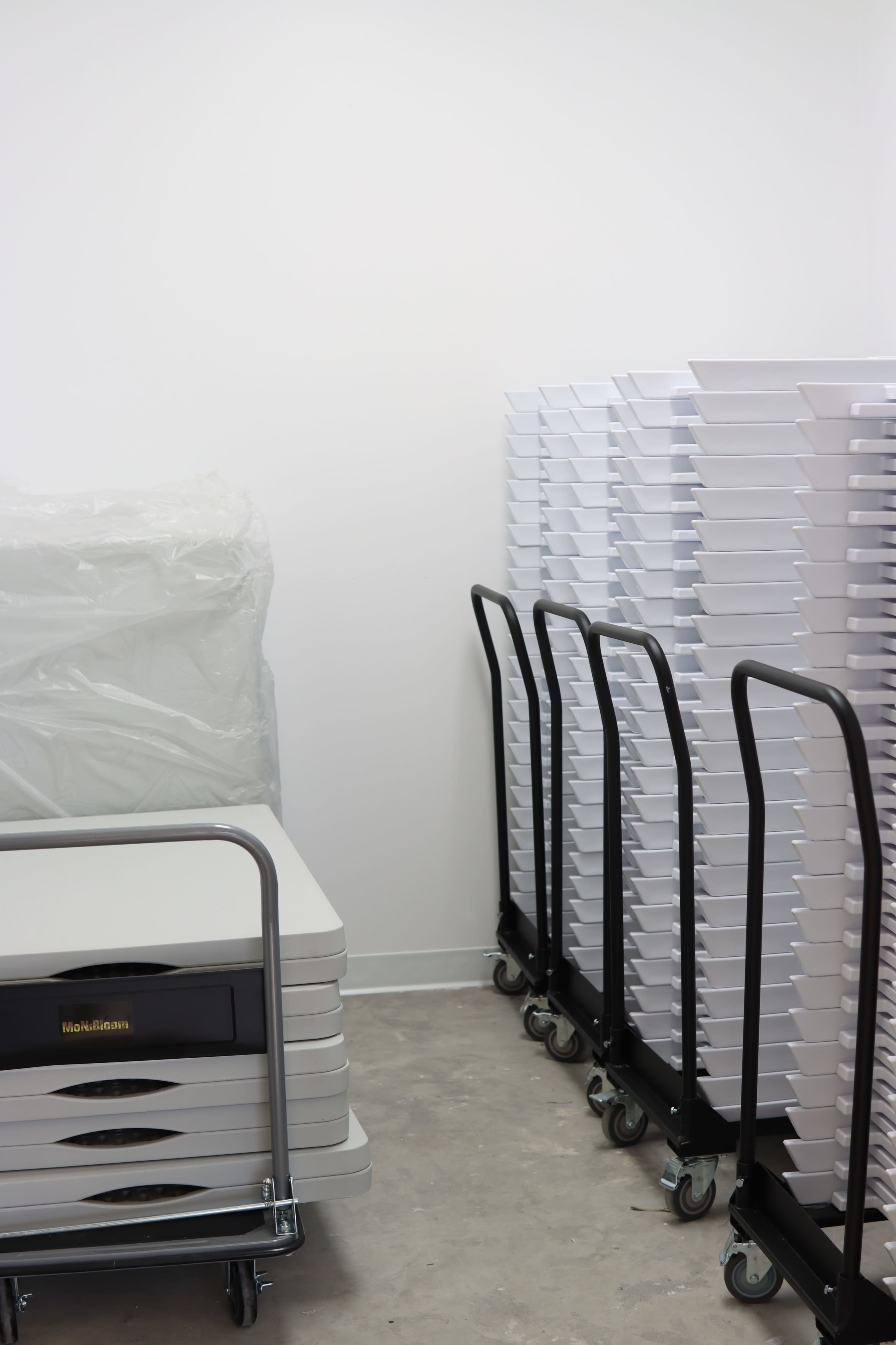 A storage area with stacked white trays on carts and a large wrapped item in the corner.