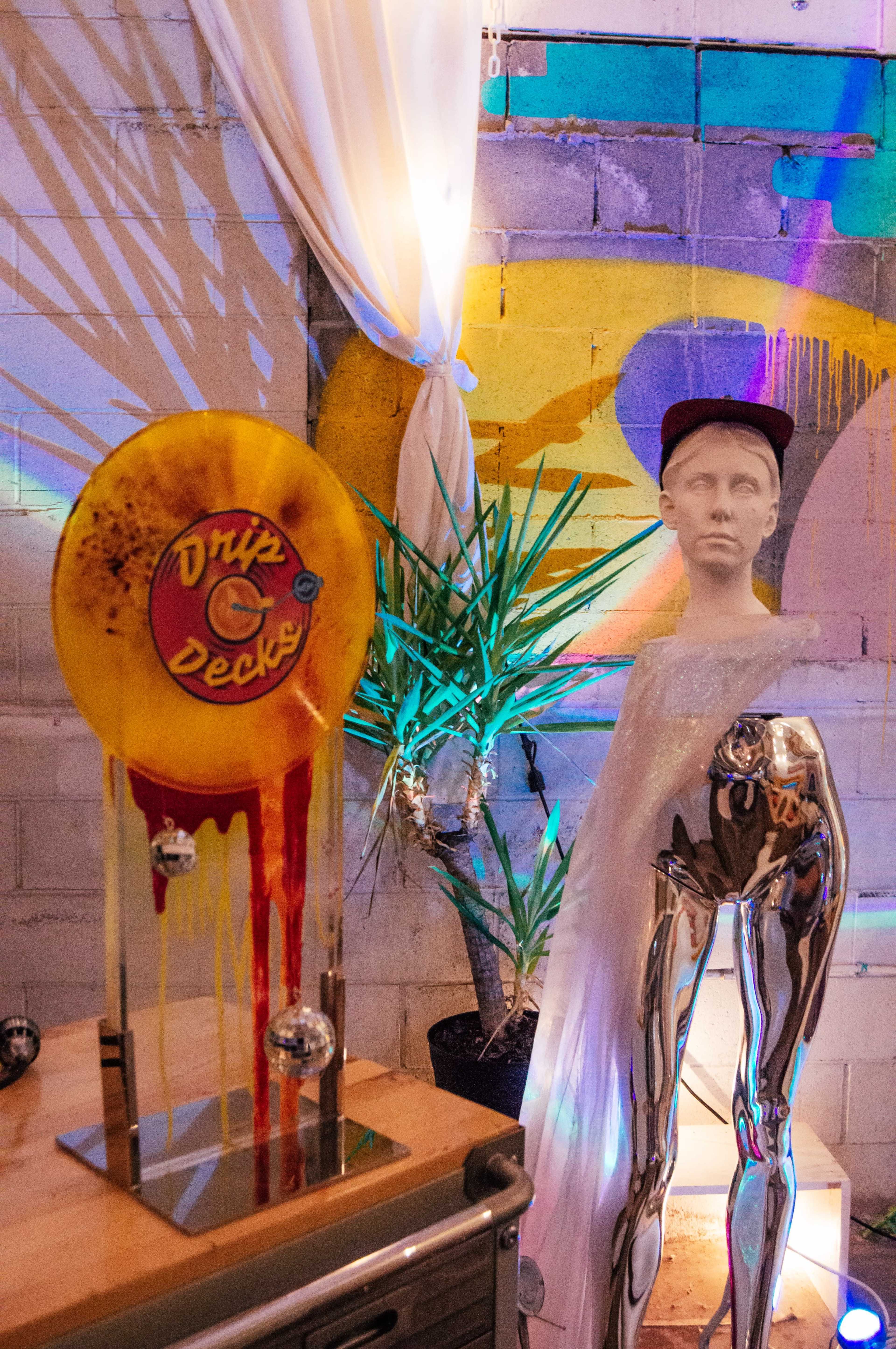 A colorful, abstract mural serves as a backdrop for a decorative display featuring a vibrant, stylized record and a silver mannequin in a contemporary setting.