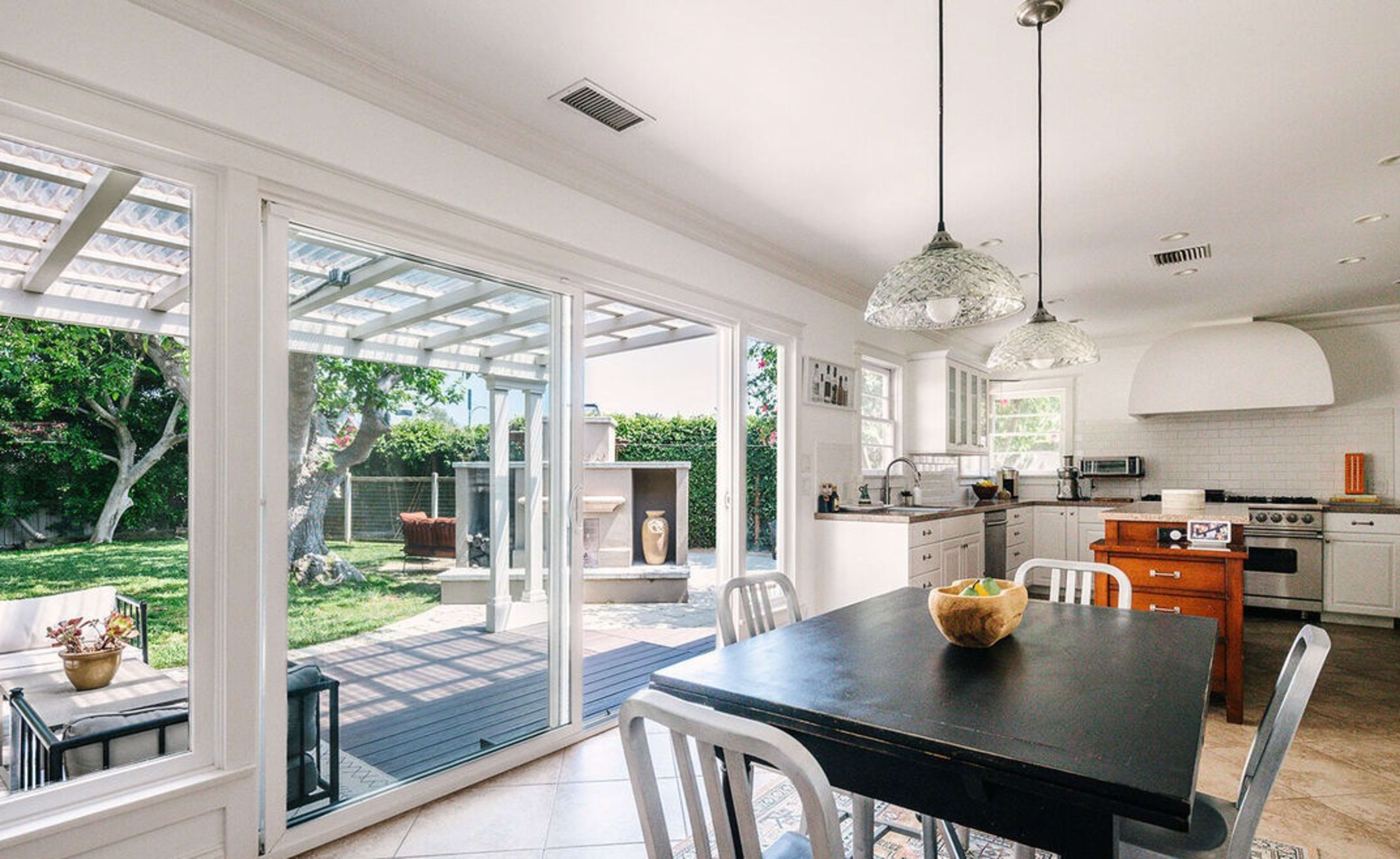 A modern kitchen features a table with black chairs, white cabinets, and sliding glass doors leading to a patio area with greenery.