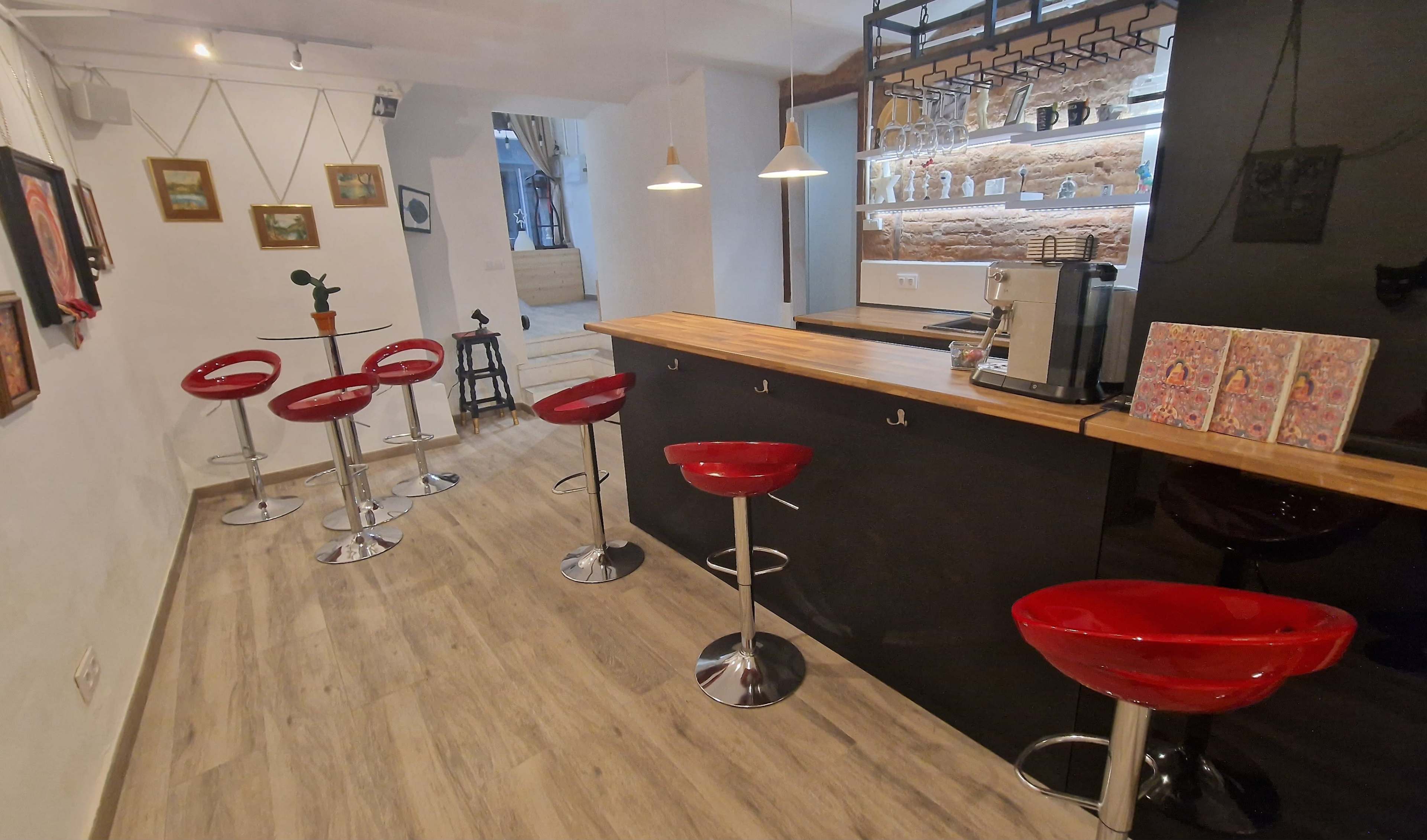 A modern café interior featuring a sleek black bar counter with wooden accents, surrounded by several red bar stools and decorative wall art.