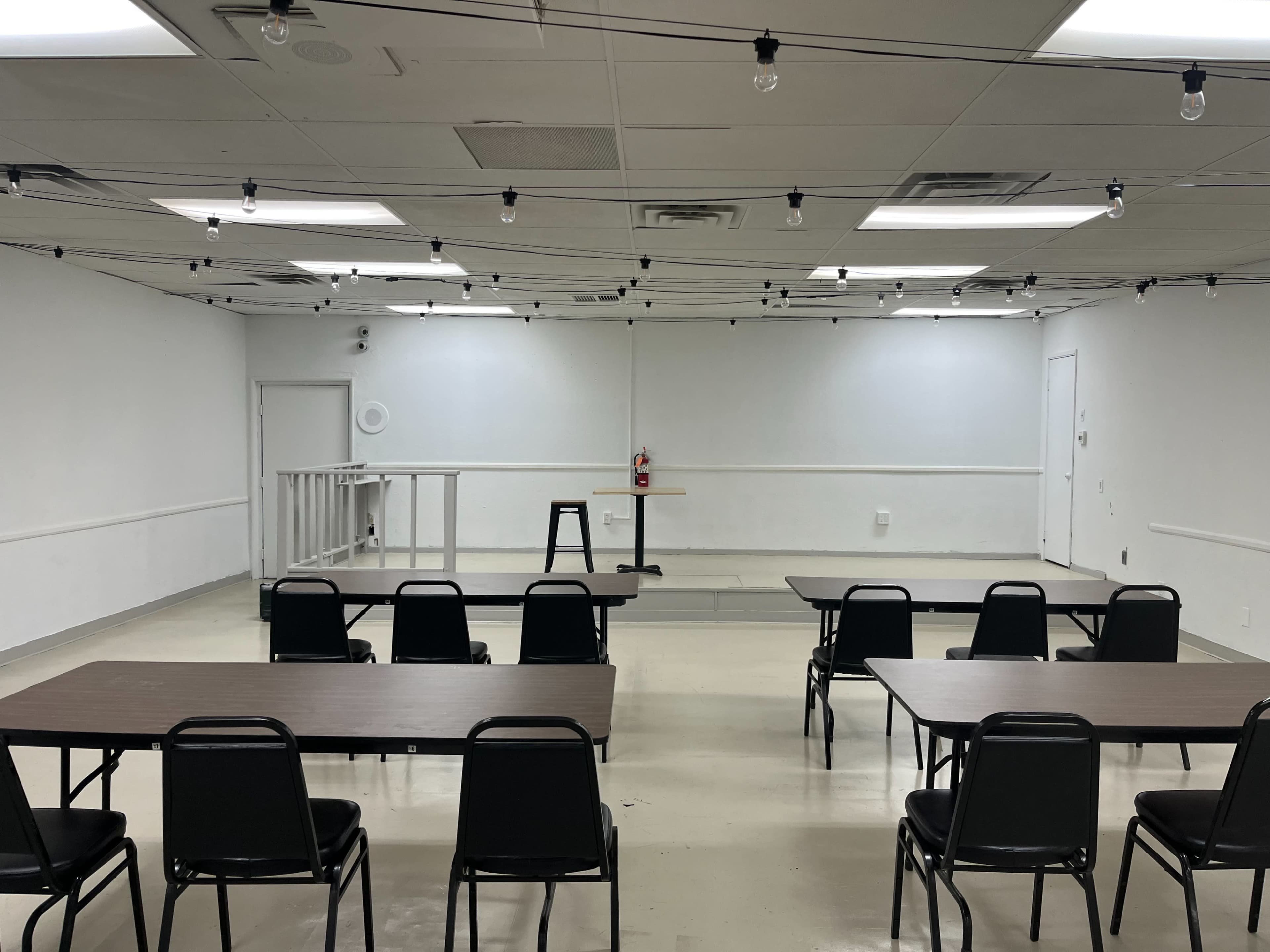 A spacious, empty room arranged with several tables and chairs facing a small stage with a podium at the front.