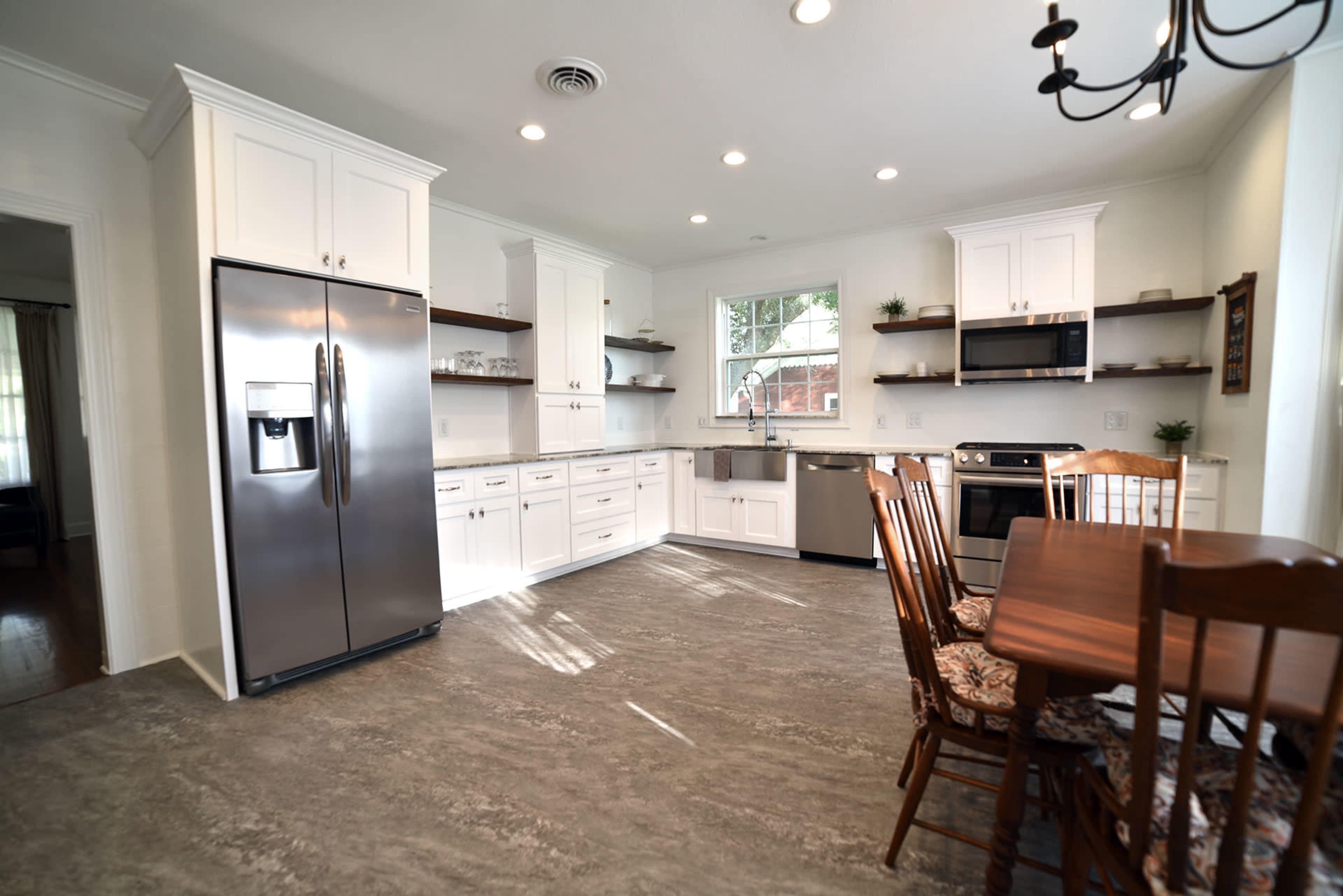 A modern kitchen features stainless steel appliances, white cabinetry, and a wooden dining table with matching chairs.