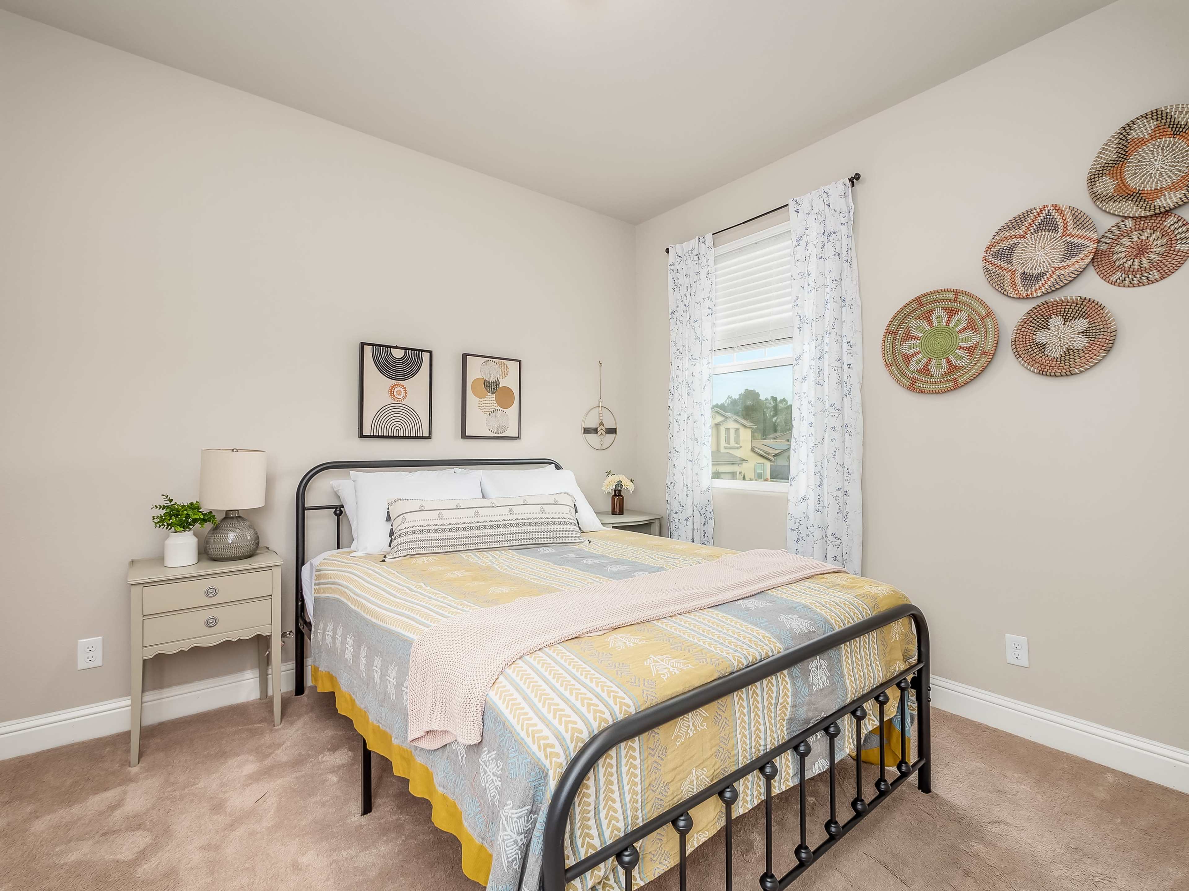 A bedroom featuring a bed with a patterned comforter, a nightstand with a lamp, and decorative wall hangings.