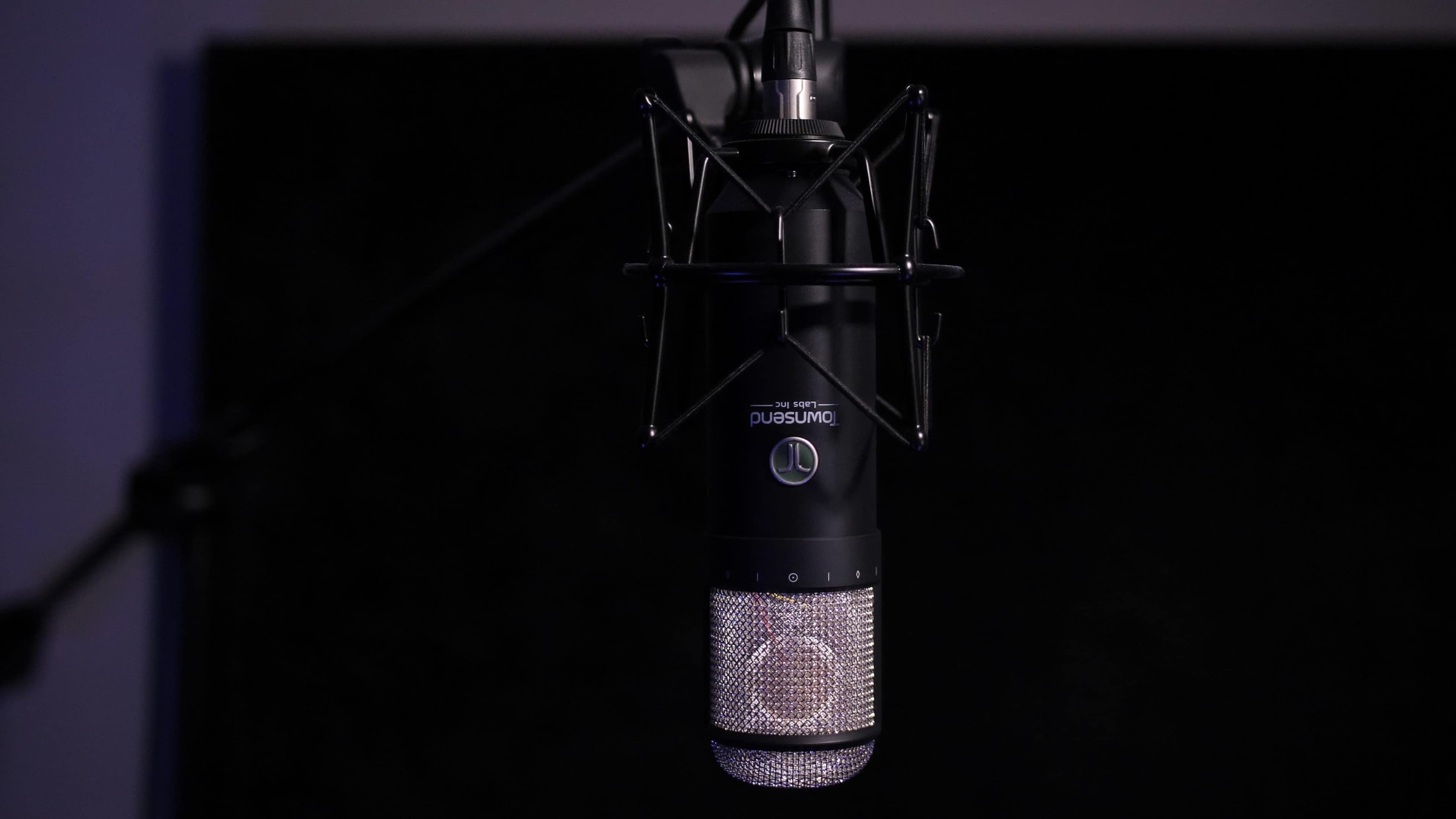 A black studio microphone hangs against a dark background.