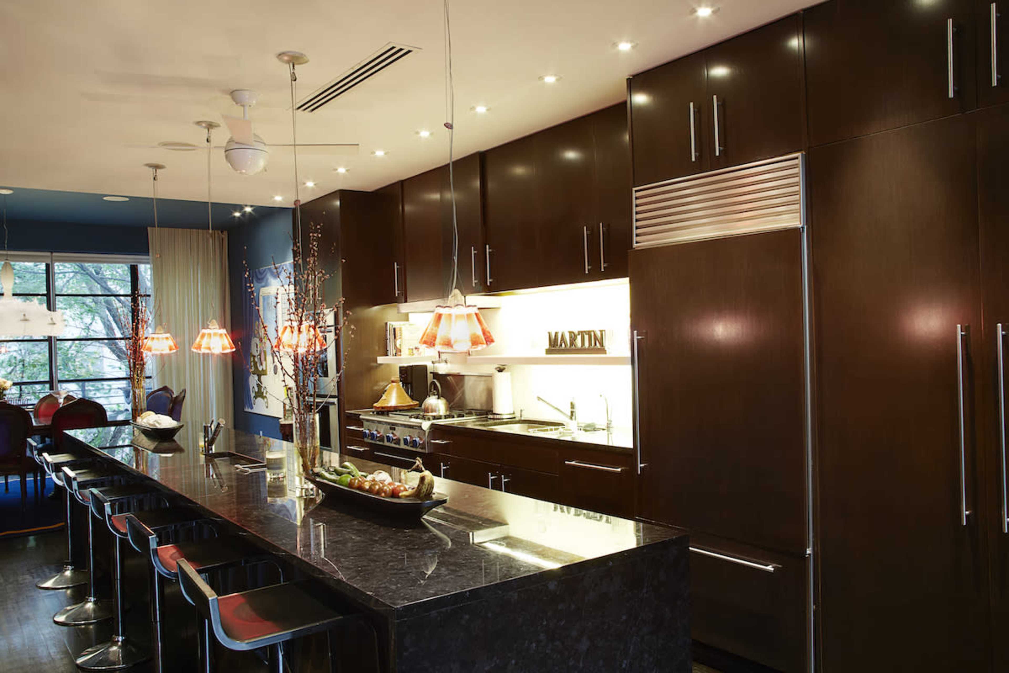 A modern kitchen with dark wood cabinetry, a large black countertop island with bar stools, and pendant lighting.