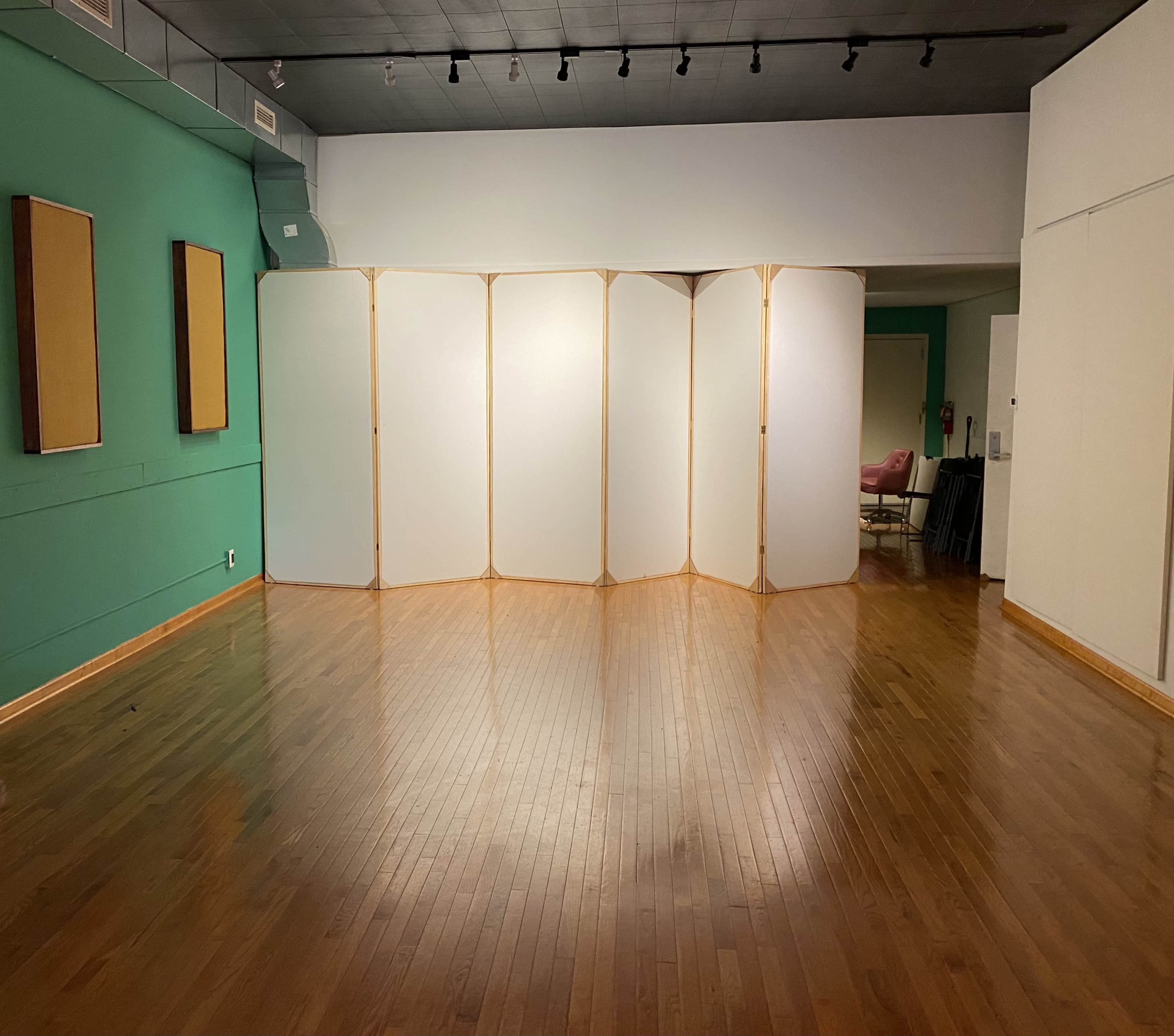 The image shows a spacious room with hardwood floors, featuring a folding screen at its center and green walls.