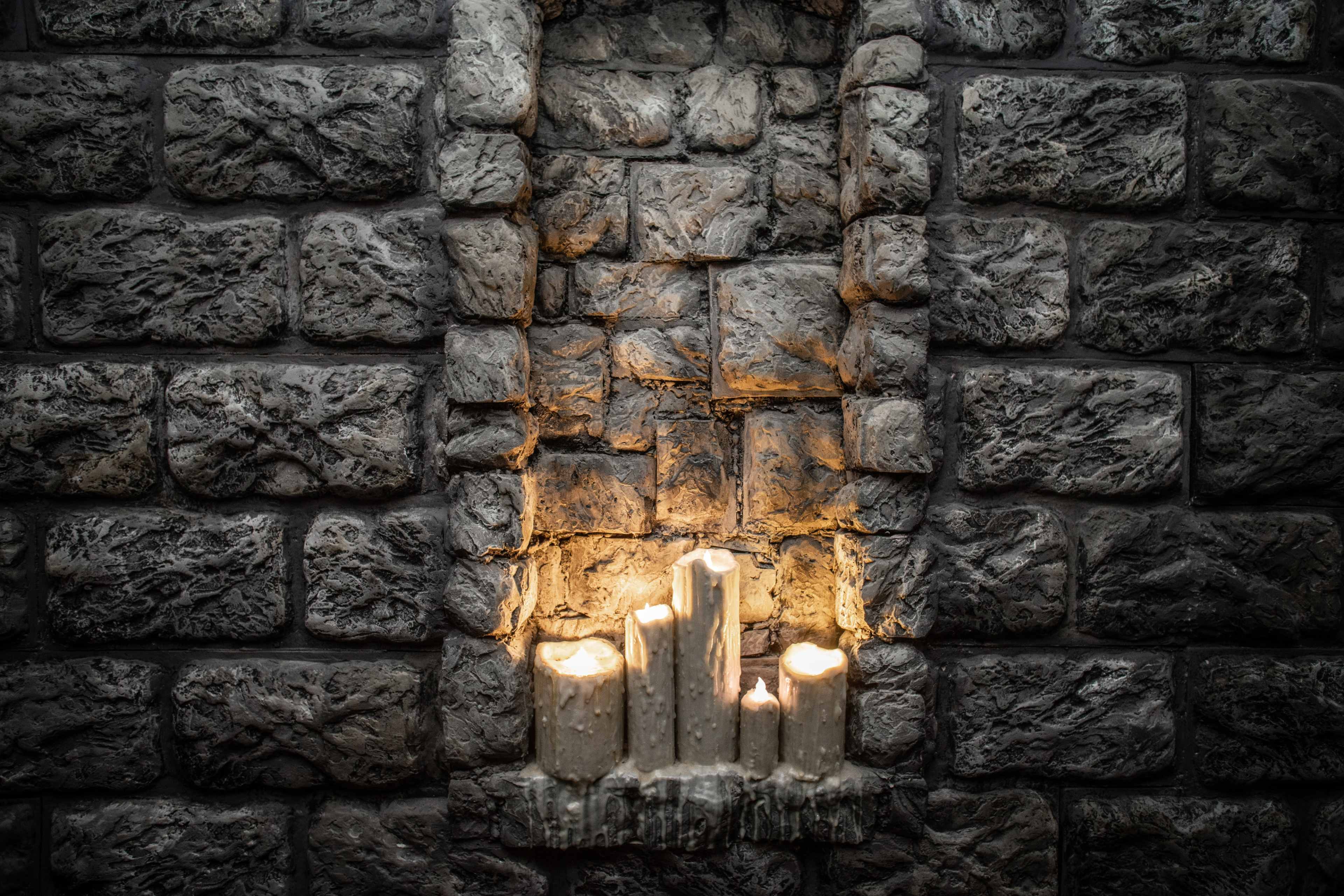 A stone wall with a recessed area containing several lit candles.