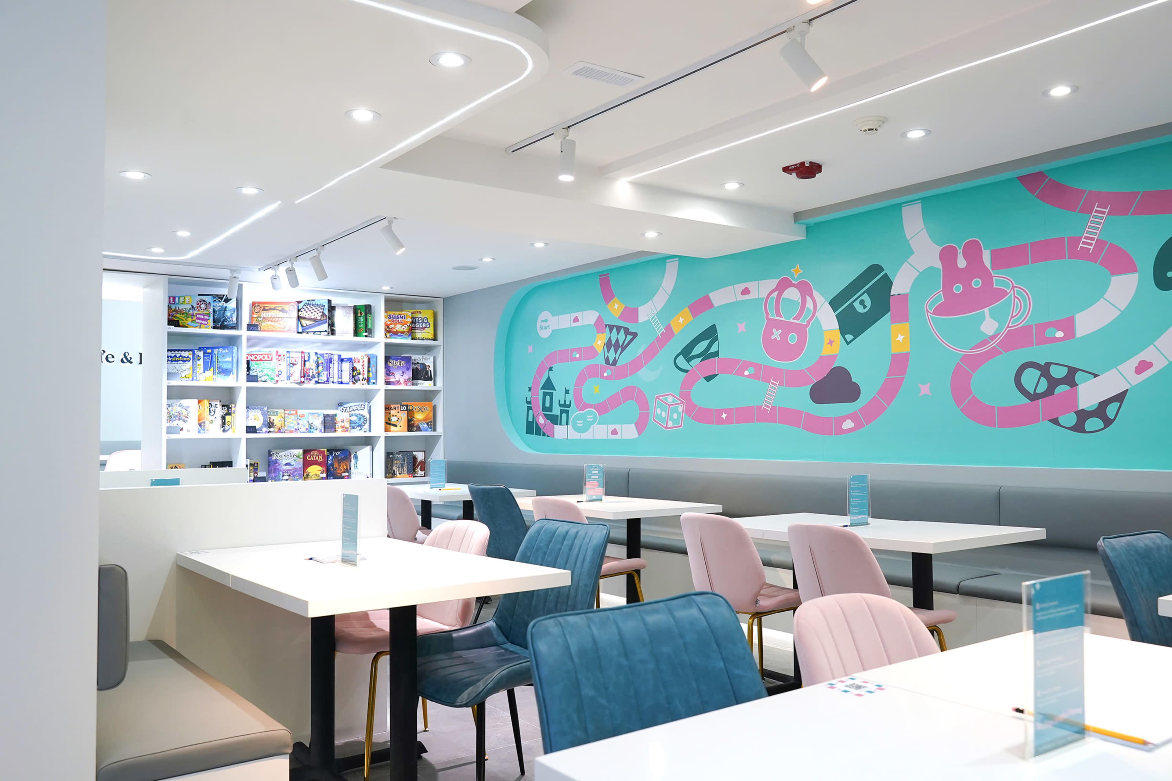 The image shows a modern café interior with colorful walls featuring playful illustrations and neatly arranged tables and chairs.