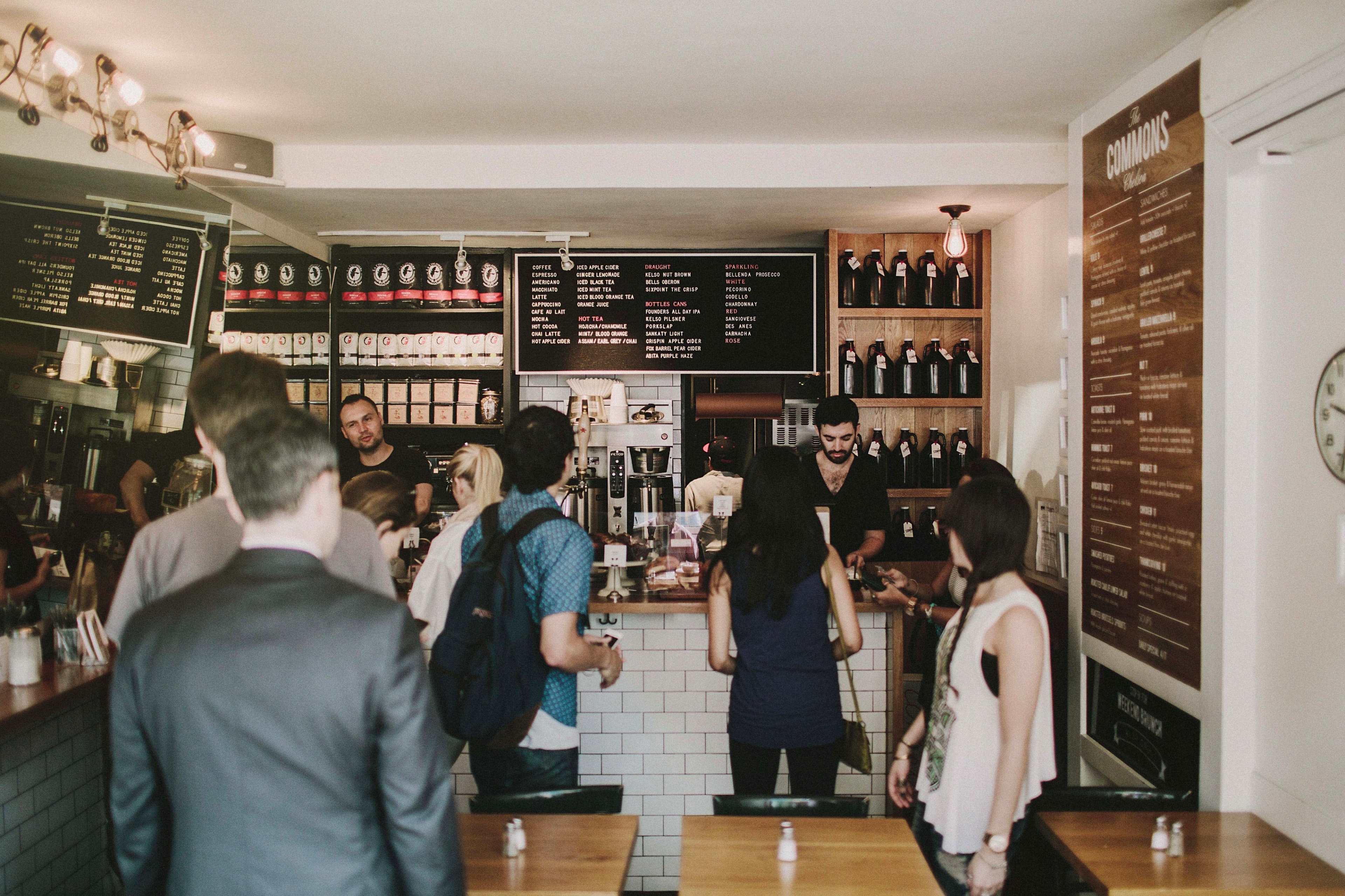A group of customers engages with staff at a coffee shop counter while others wait in line.