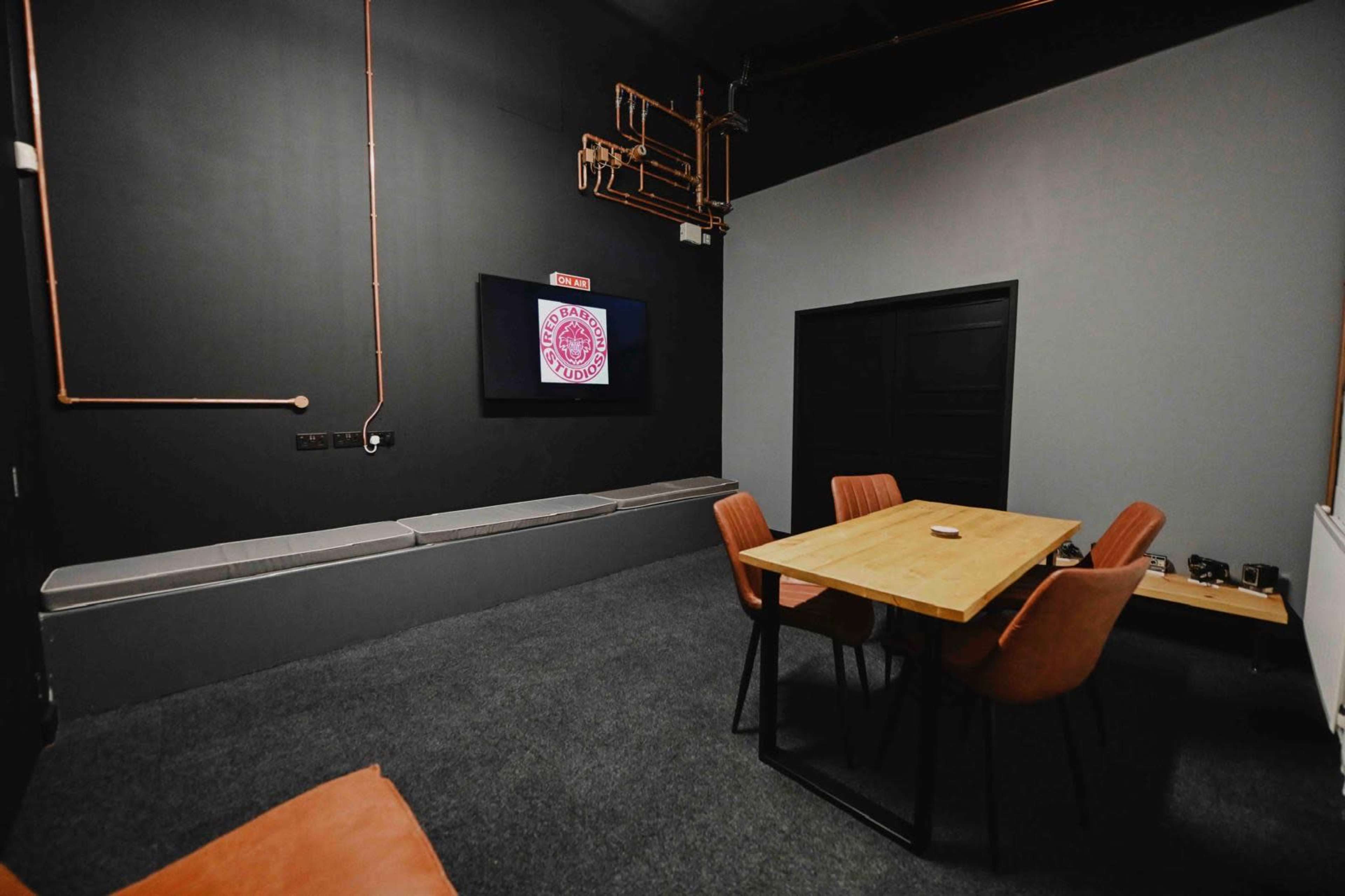 A small meeting room with a wooden table and orange chairs, black walls, and a screen mounted on the wall.