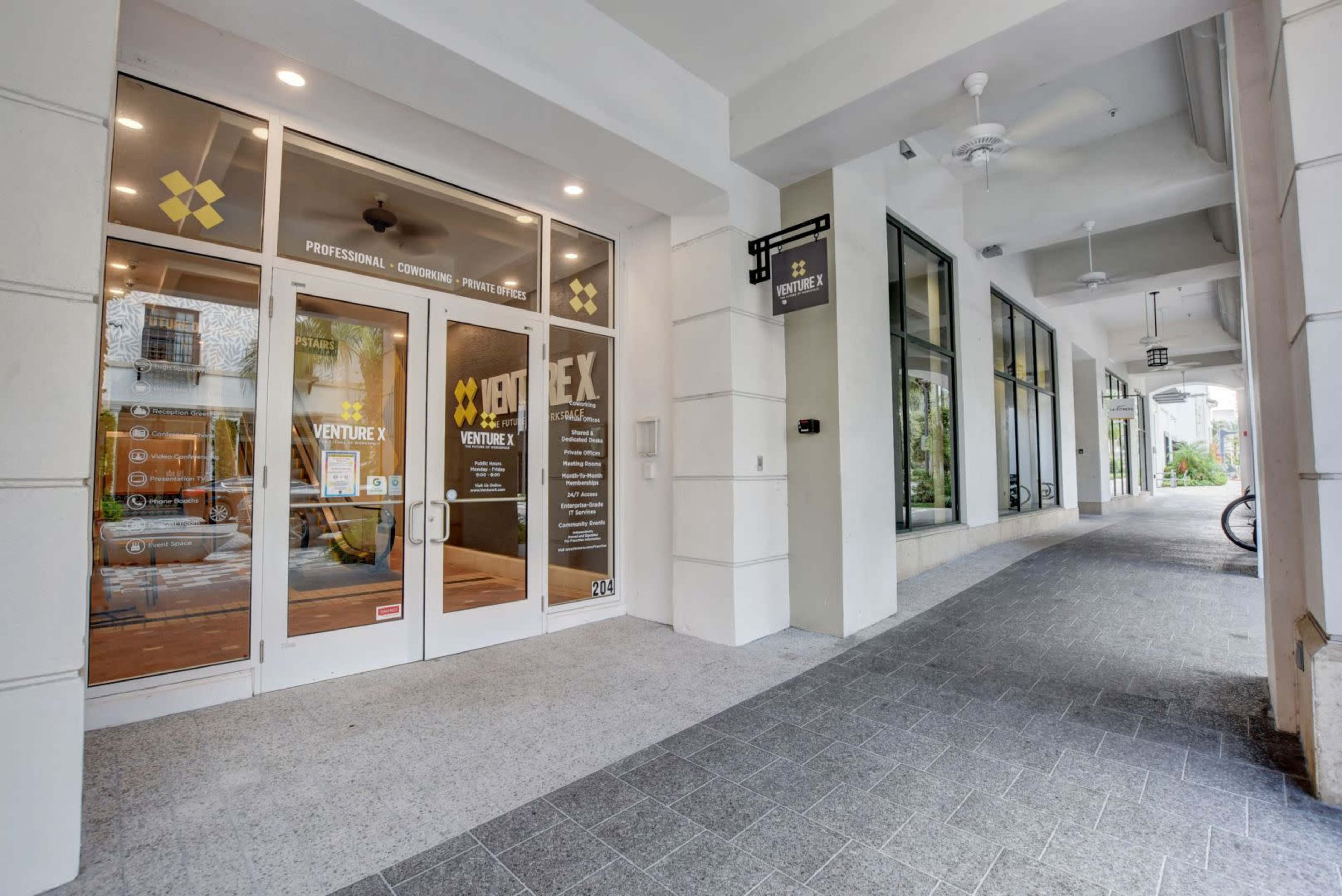 The entrance of a co-working space named Venture X, featuring large glass doors and a well-maintained sidewalk outside.