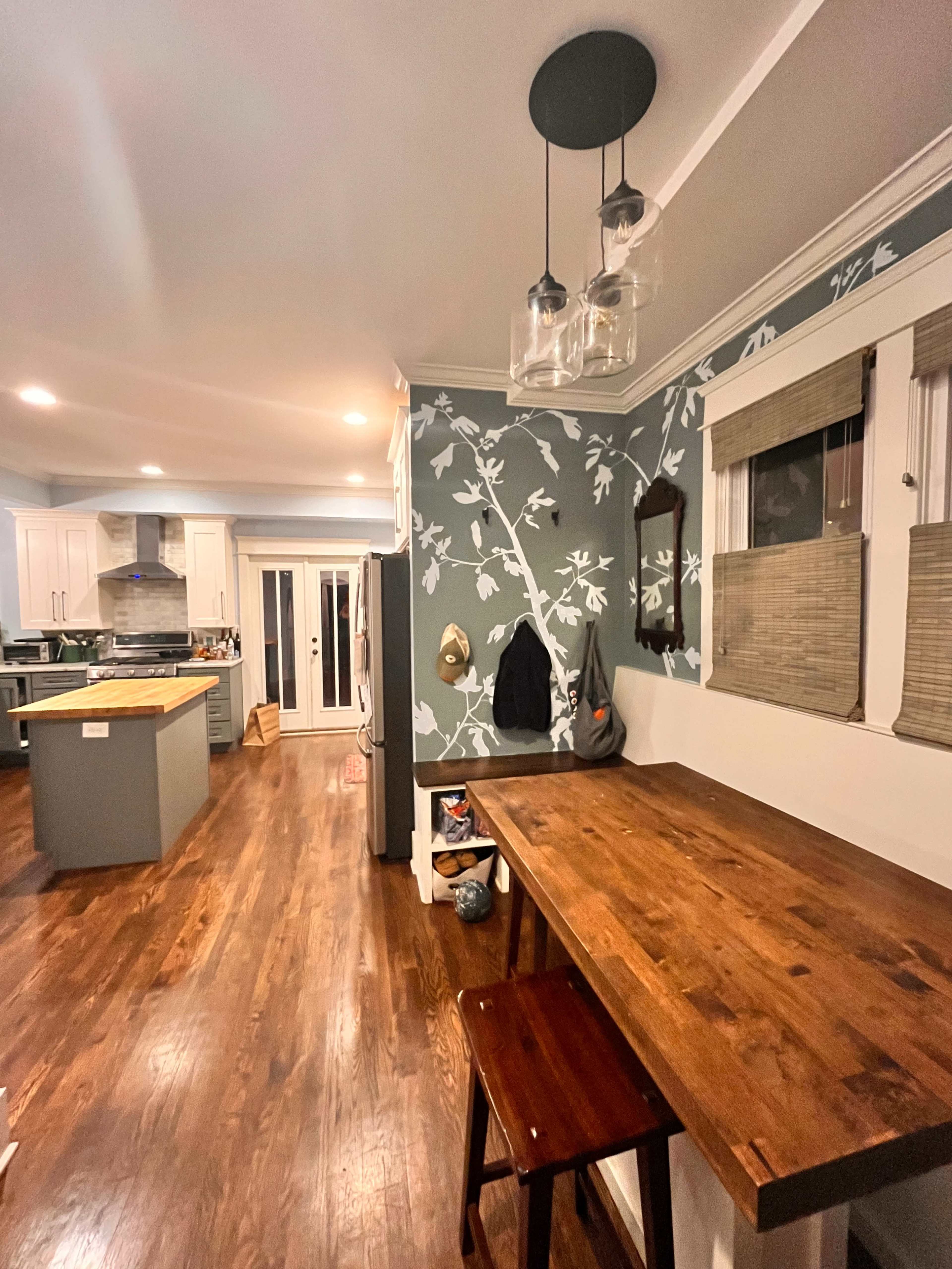 A kitchen with a wooden table, blue and white patterned wallpaper, and hanging pendant lights.