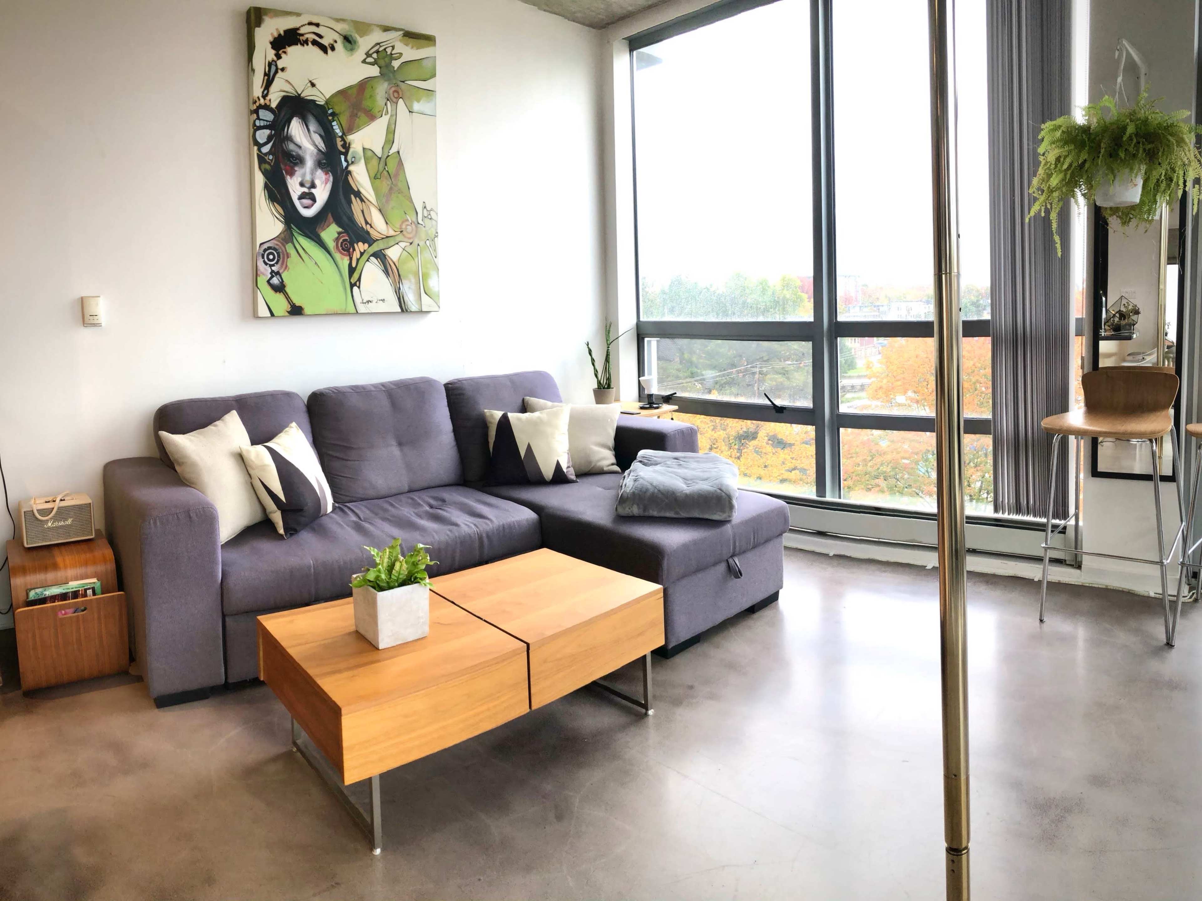 A modern living room with a gray sectional sofa, a wooden coffee table, and large windows that provide a view of an outdoor landscape.
