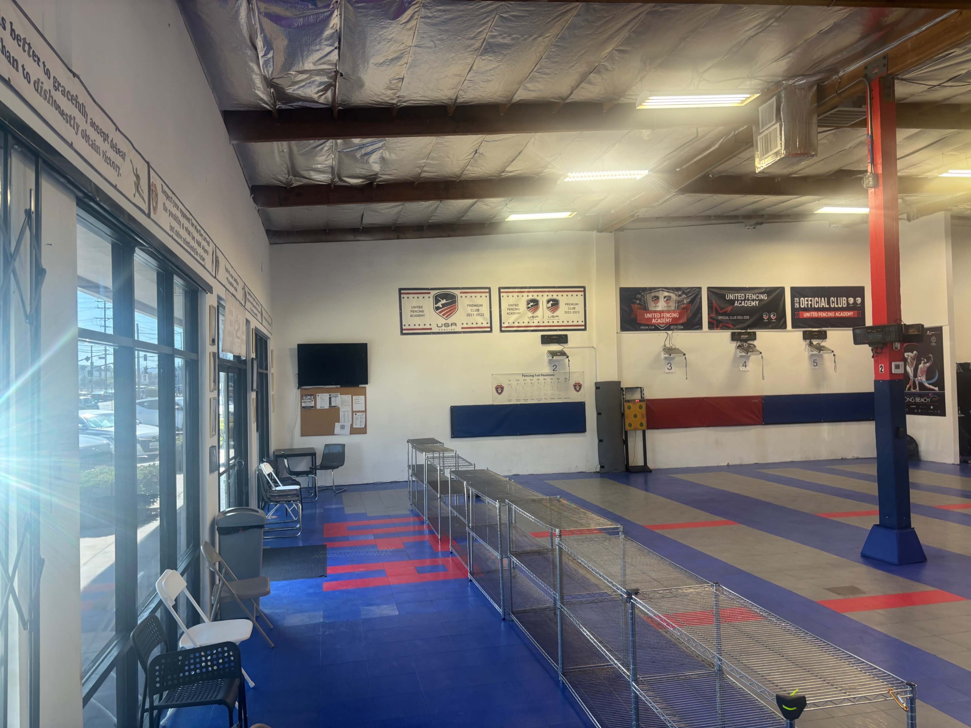 The image shows an indoor training facility with blue and red flooring, wall-mounted banners, and a seating area along one side.