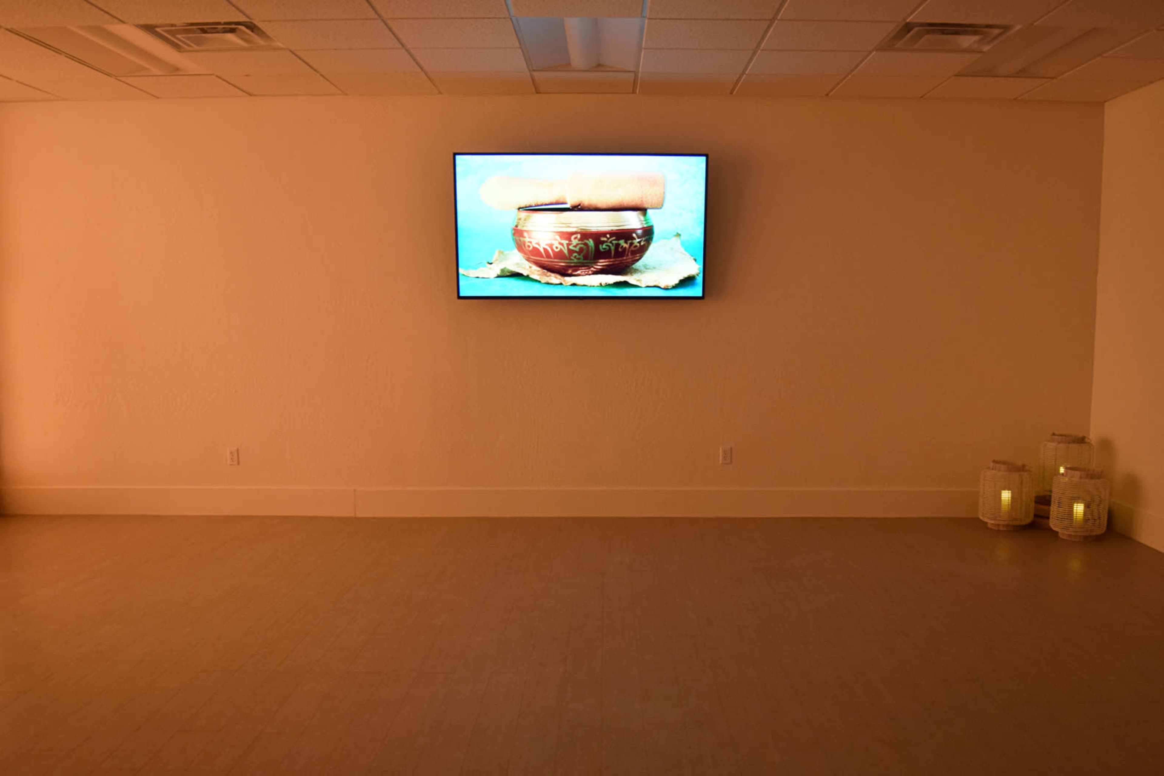 A large screen displays an image of a bowl on a wall in a sparsely furnished room with soft lighting.
