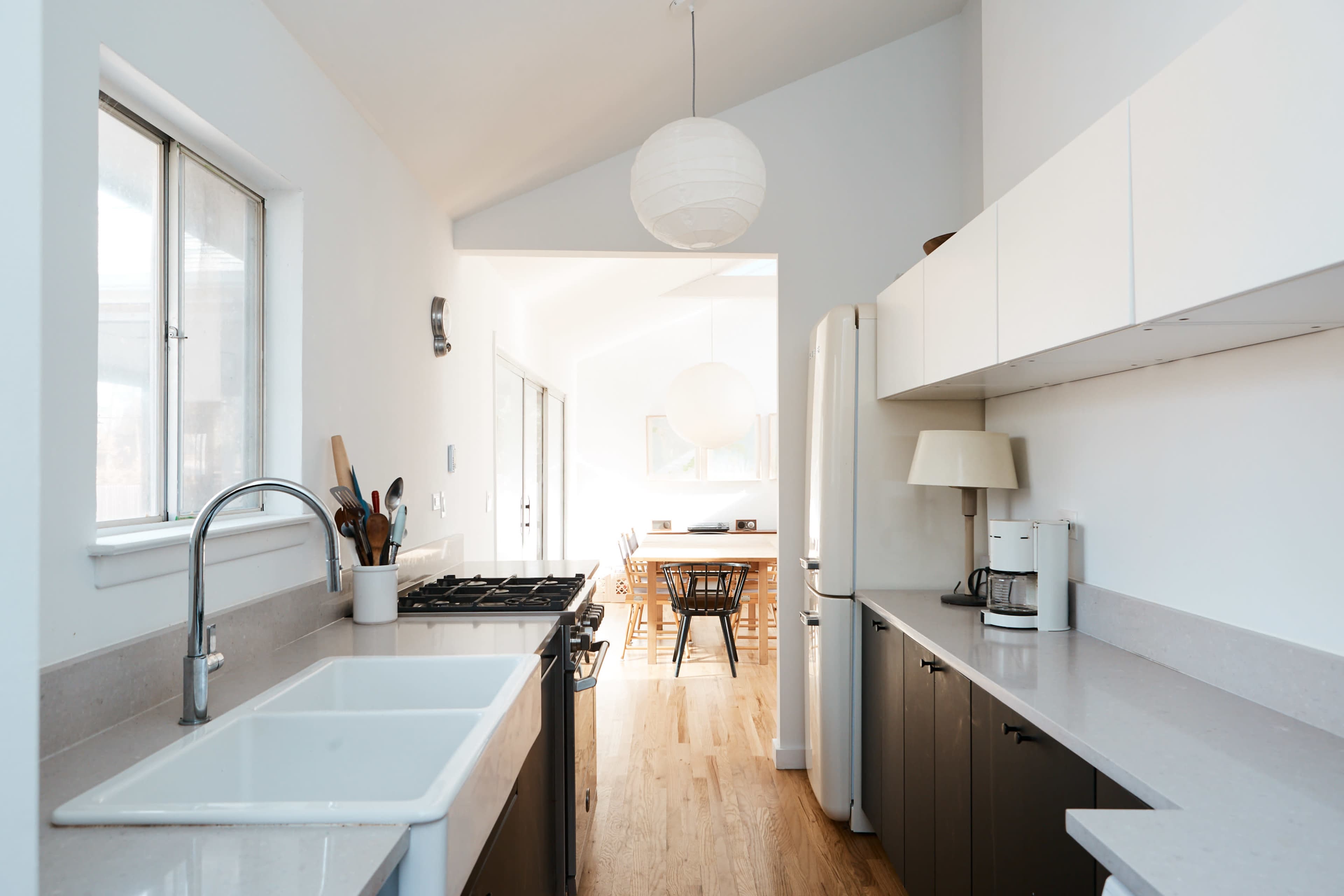 A modern kitchen features a large sink, a stove, and minimalist cabinetry with a doorway leading to a dining area.
